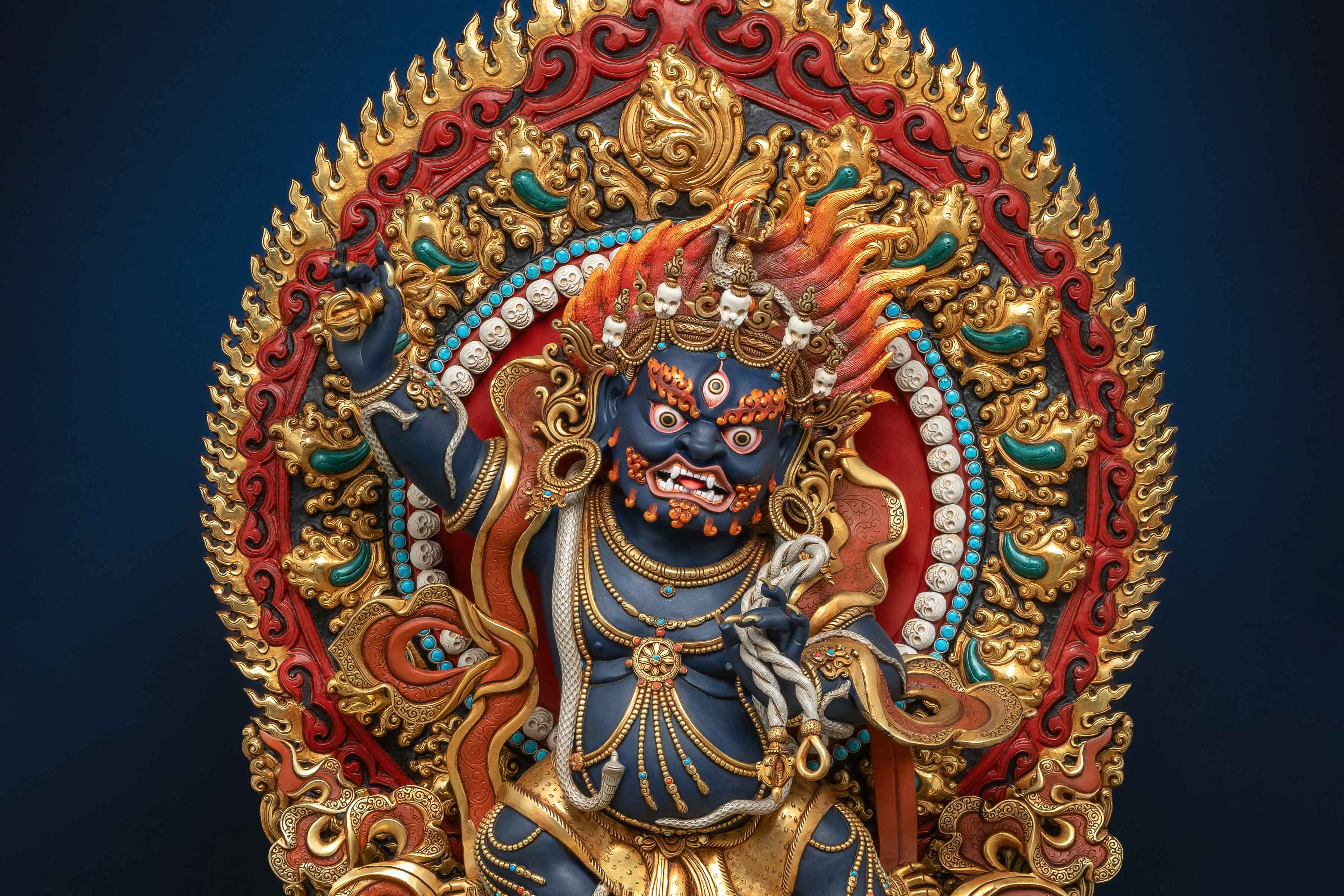 statue of fierce wrathful deity vajrapani who has black skin and has red fiery fire at the back with gold accents throughout the statue