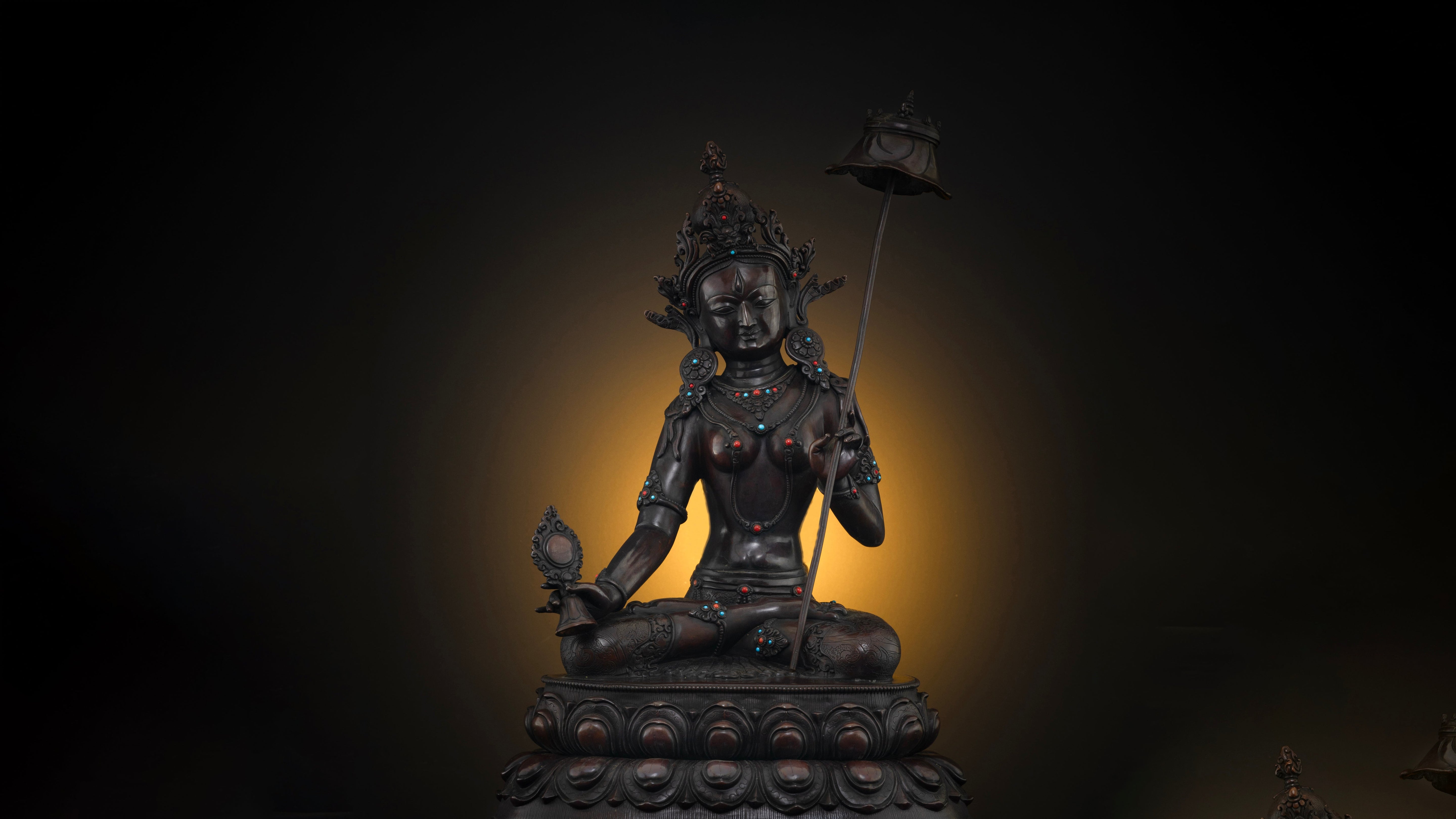 Oxidized copper dark brown statue of Dukkar with a dark background with a golden glow