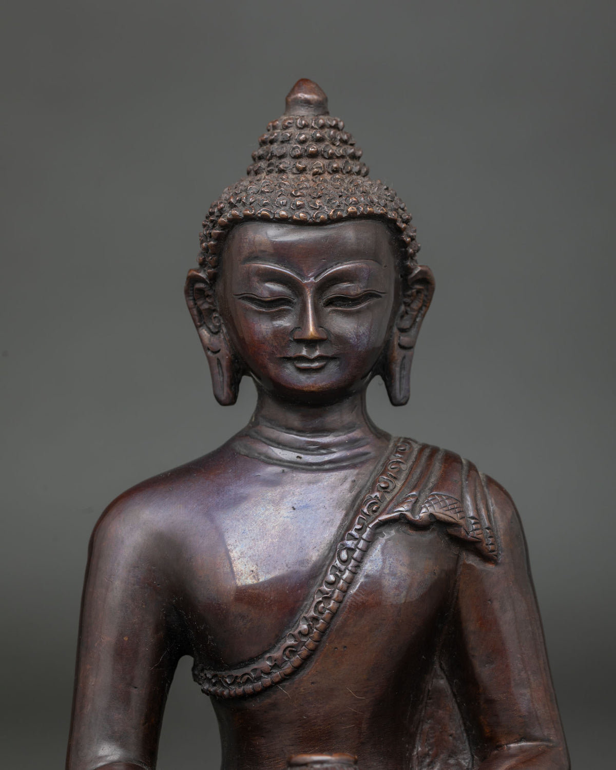 Close-up of Amitabha Buddha copper statue showing serene face, curled hair and carved shoulder drape