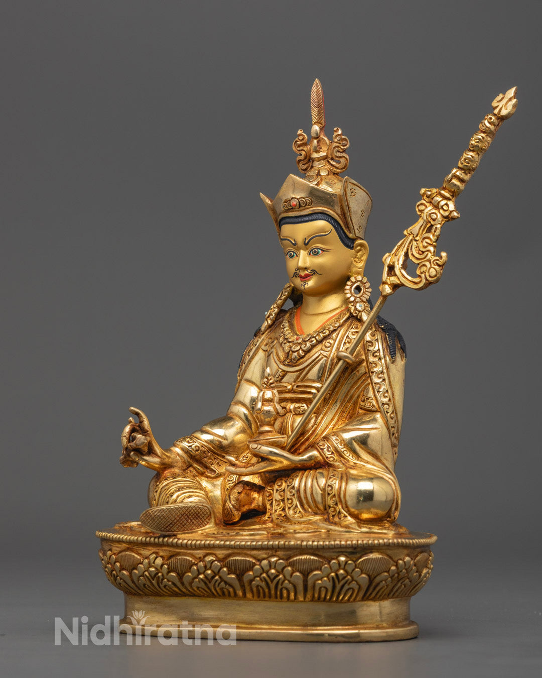 Artistic representation of Guru Rinpoche holding vajra and skull cup, surrounded by symbolic flames, showcasing hand-carved details and spiritual symbolism.