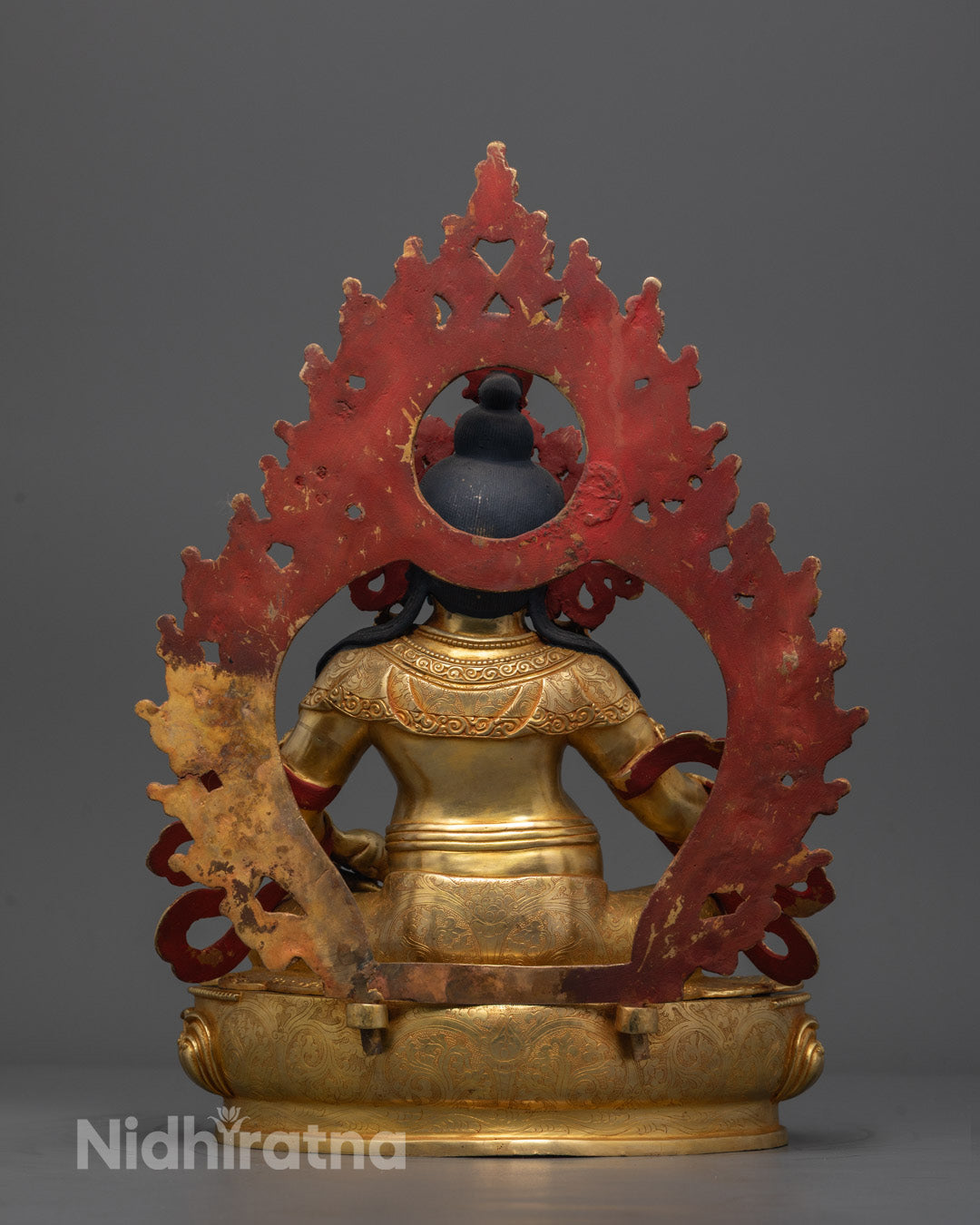 Back angle of Dzambhala sculpture highlighting detailed carvings on flowing robe and halo.
