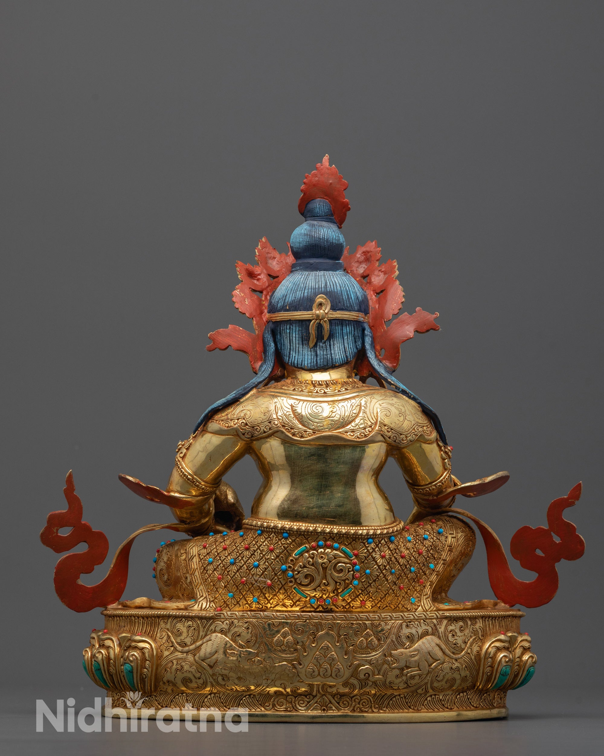 Back view of Dzambhala statue with hand-carved two mongooses near shell on lotus seat