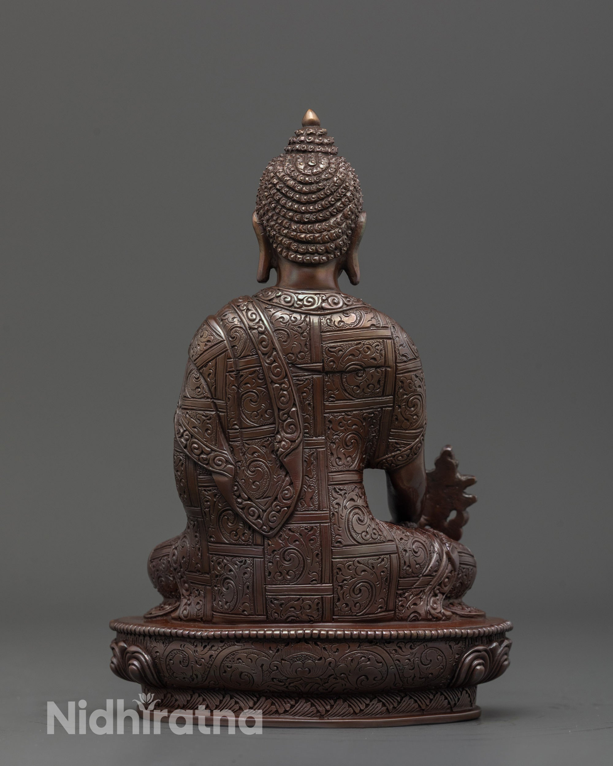 Back view of Medicine Buddha statue revealing detailed monk’s robe and oxidized copper finish