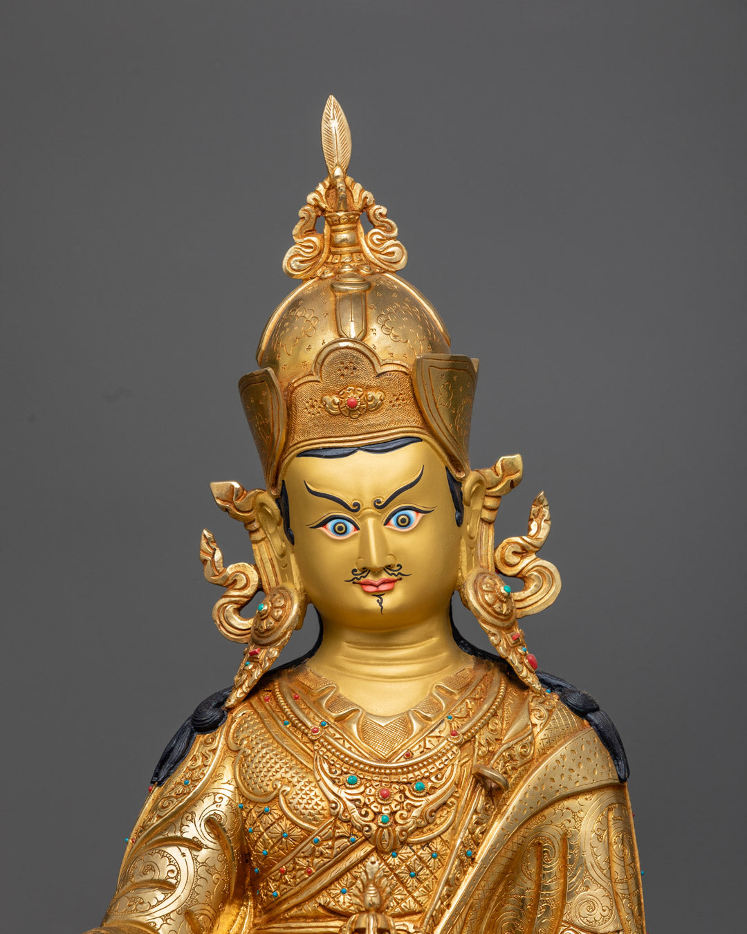 Beautifully decorated Guru Rinpoche statue adorned with semi-precious stones and vibrant acrylic colors on crown and jewelry.