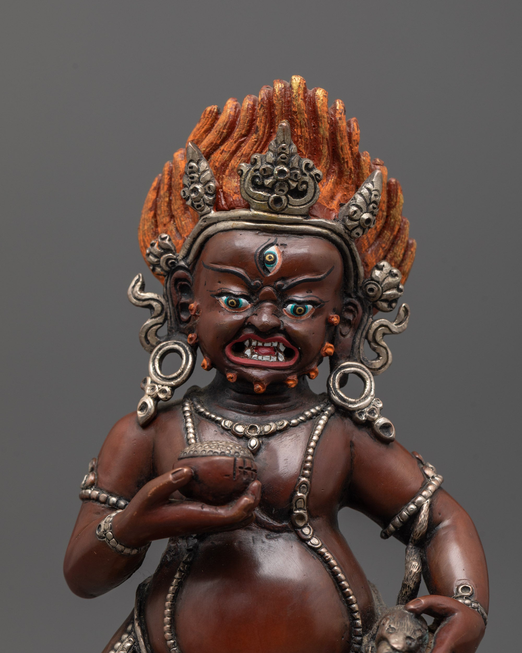 Close up of Dzambhala's fierce face and silver jewelry on oxidized copper Buddhist statue