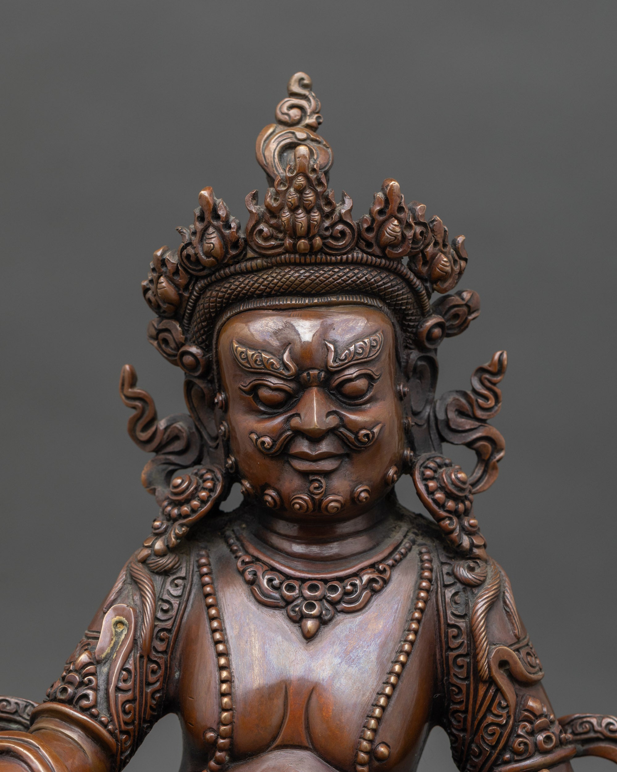 Close-up of Dzambhala deity statue showing intricate copper details and precious jewel symbolizing abundance