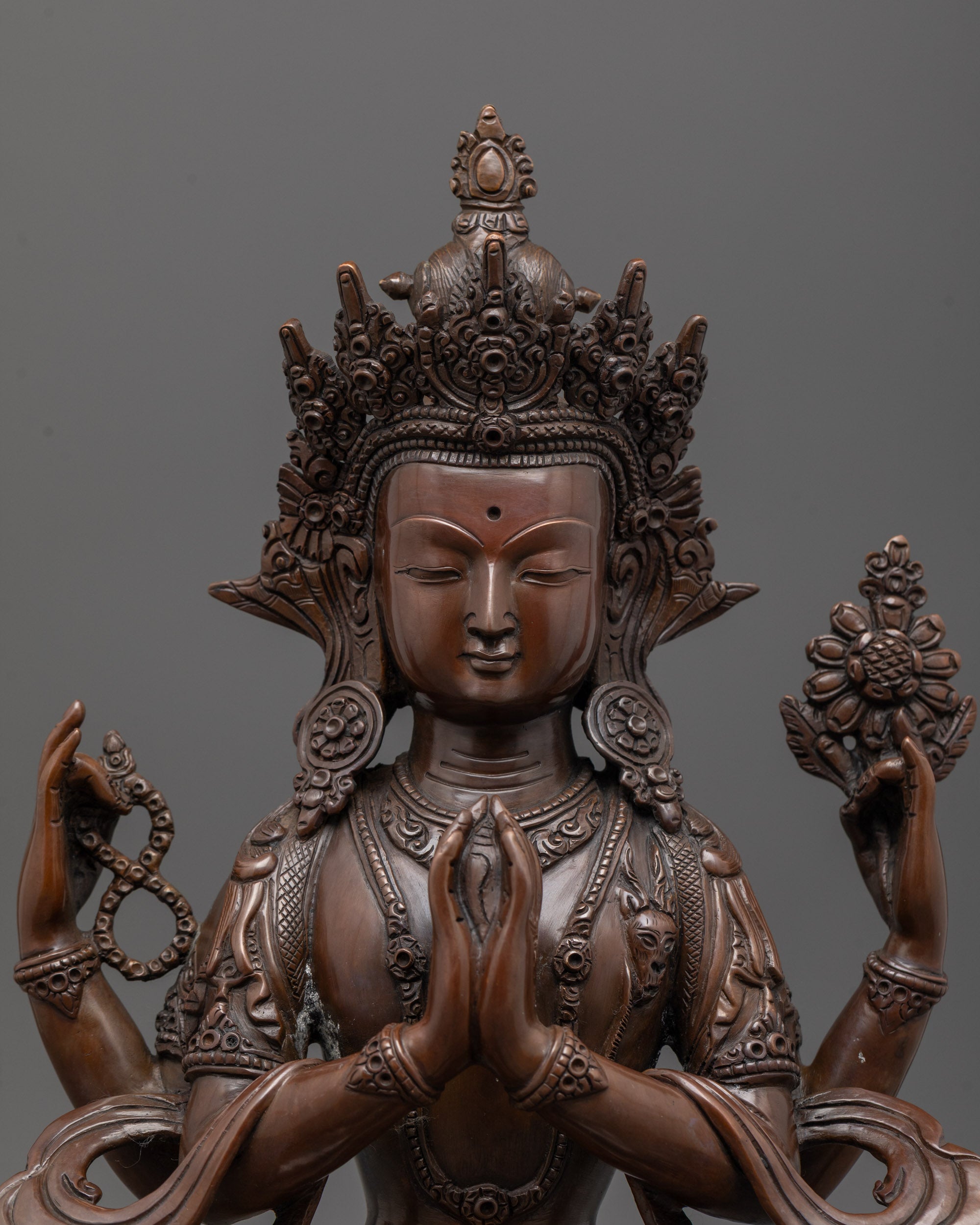 Close-up of Chenrezig statue's serene face and deer symbol beside heart, oxidized finish
