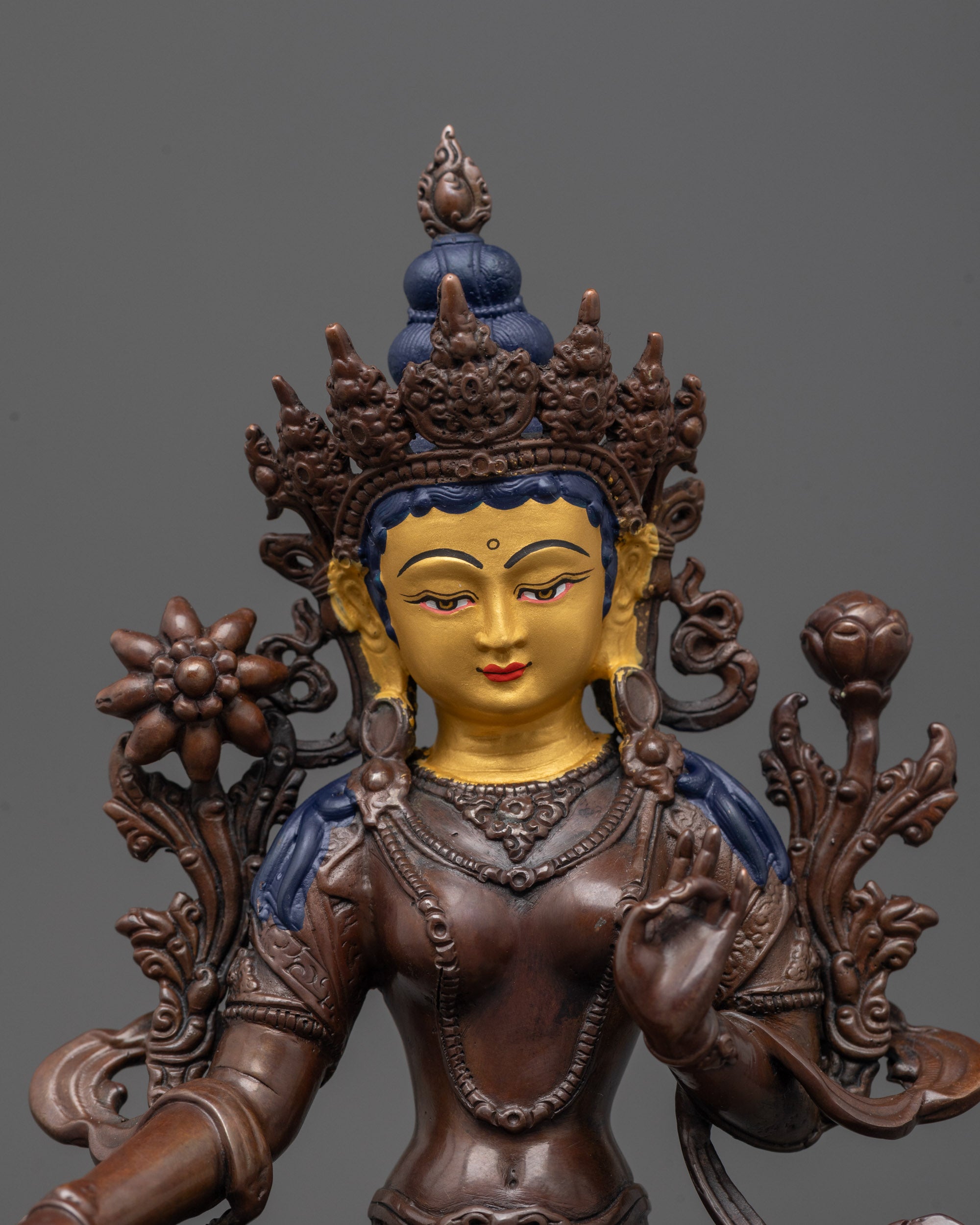 Close-up of Green Tara statue's serene gold-gilded face and detailed utpala flower carving