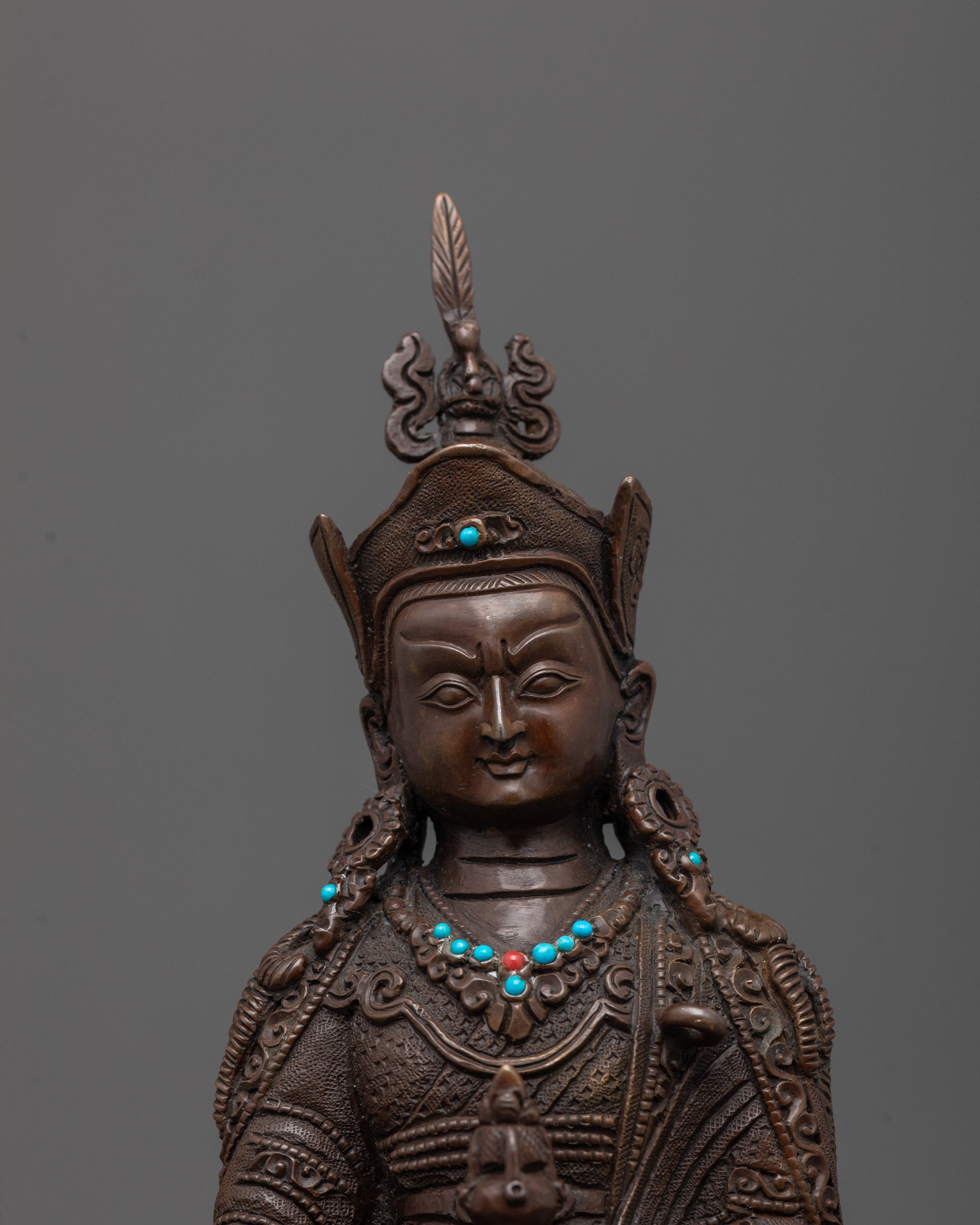 Close-up of Guru Rinpoche’s face, semi-precious stone crown, vajra, and skull cup in hand