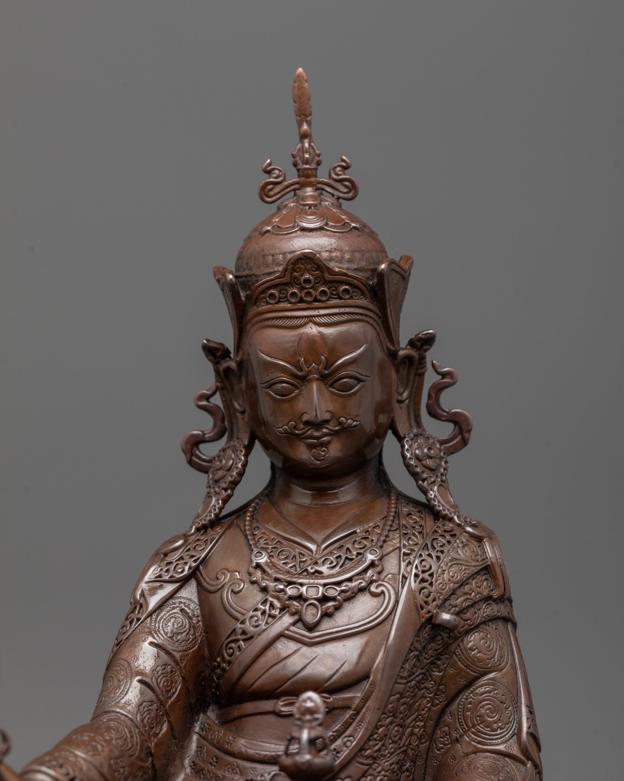 Close-up of Guru Rinpoche’s face with semi-wrathful expression and hands holding vajra