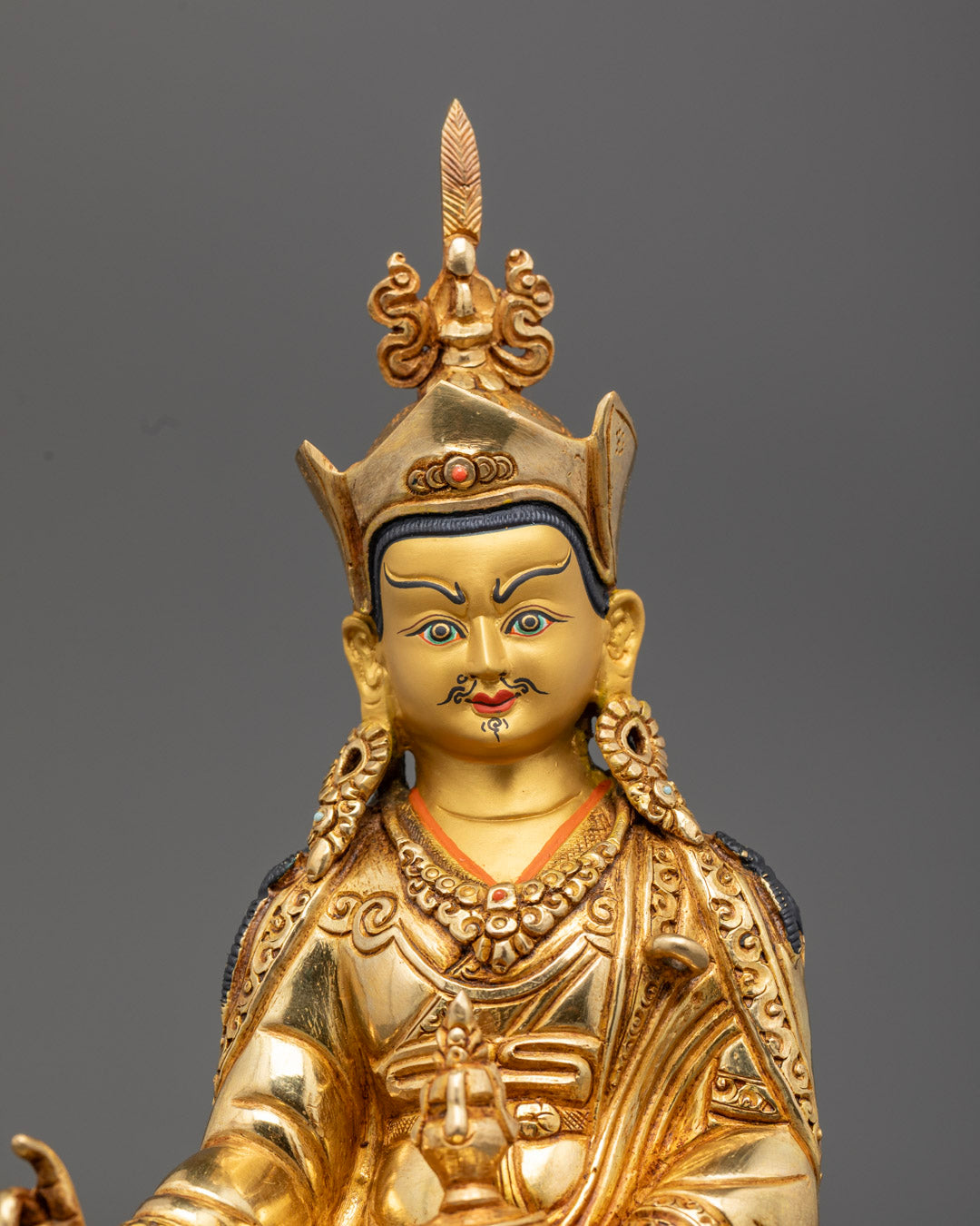Close-up of Guru Rinpoche’s serene face with gold gilding and semi-precious stone adornments, highlighting traditional Himalayan craftsmanship.
