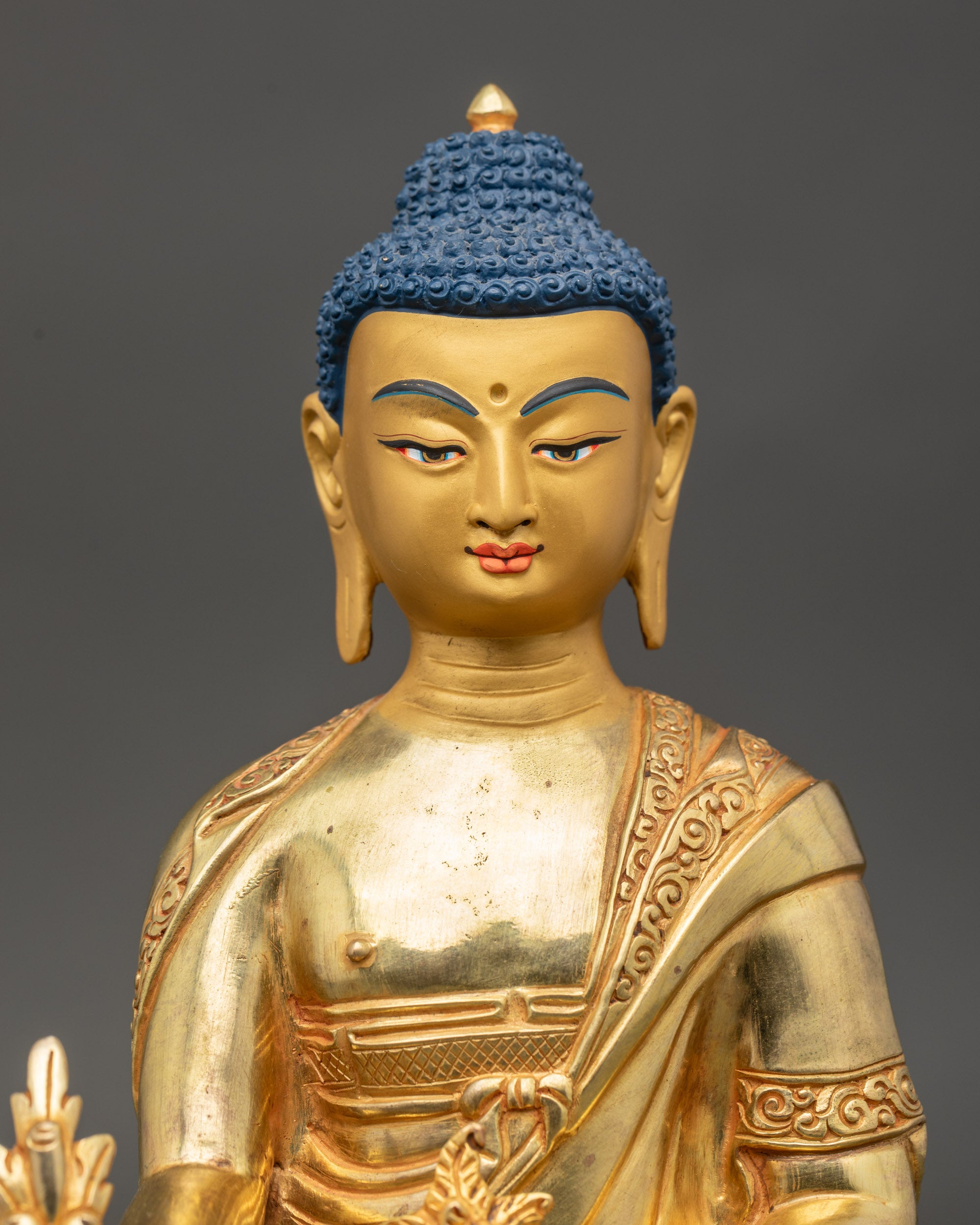 Close-up of Medicine Buddha face with serene expression and gold-painted details