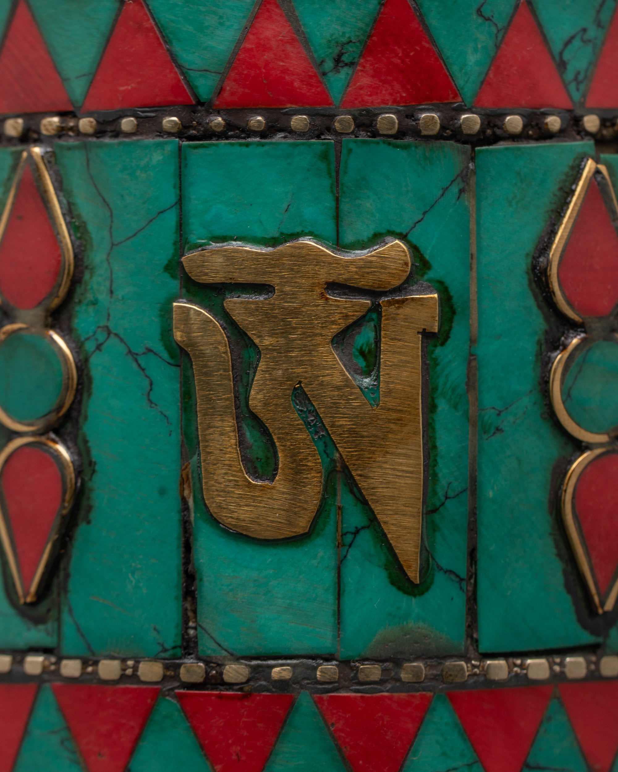 Close-up of engraved sacred mantras on copper prayer wheel with turquoise and coral inlays