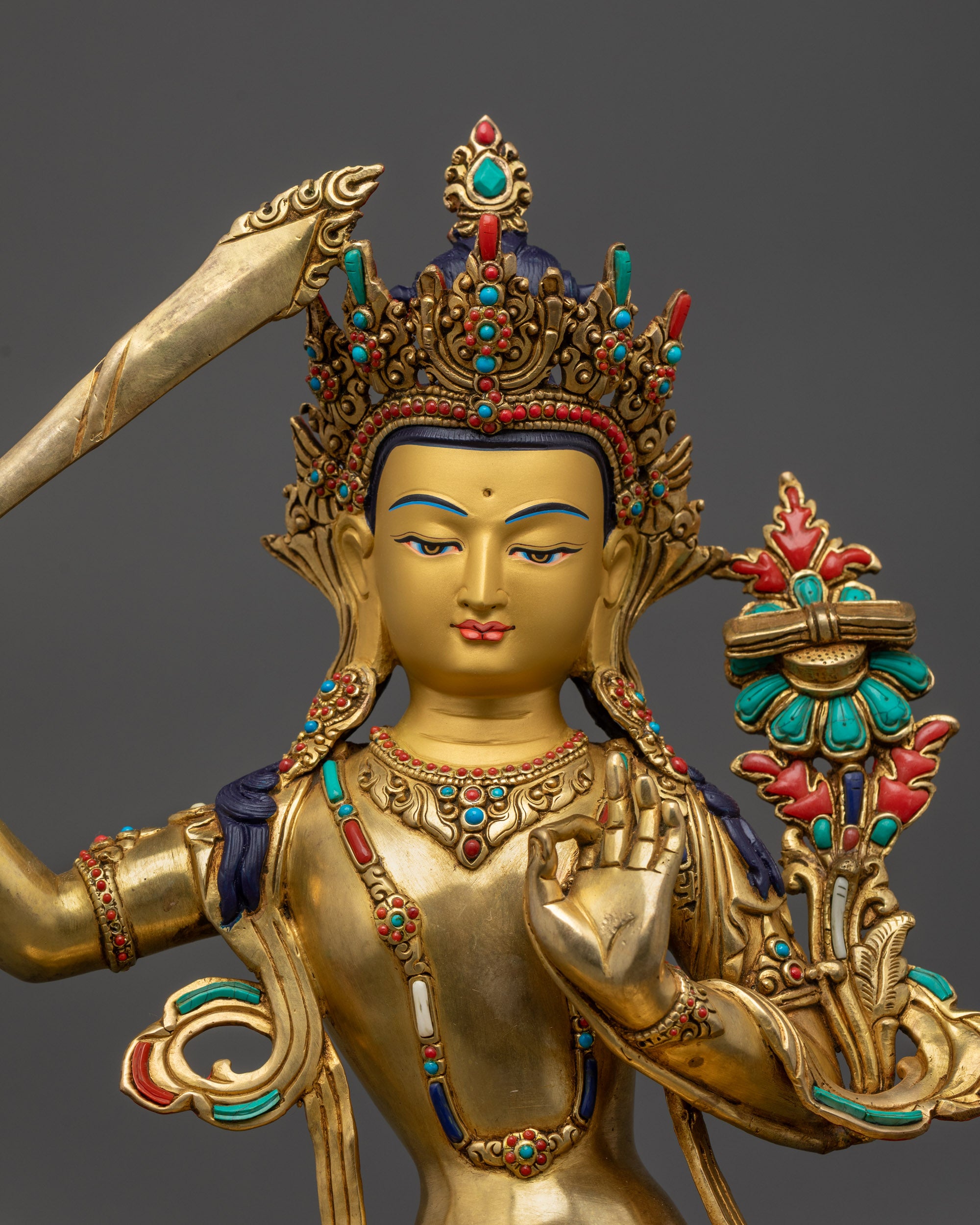 Close-up of gold-gilded Manjushri face holding utpala flower and flaming sword symbolizing divine wisdom.