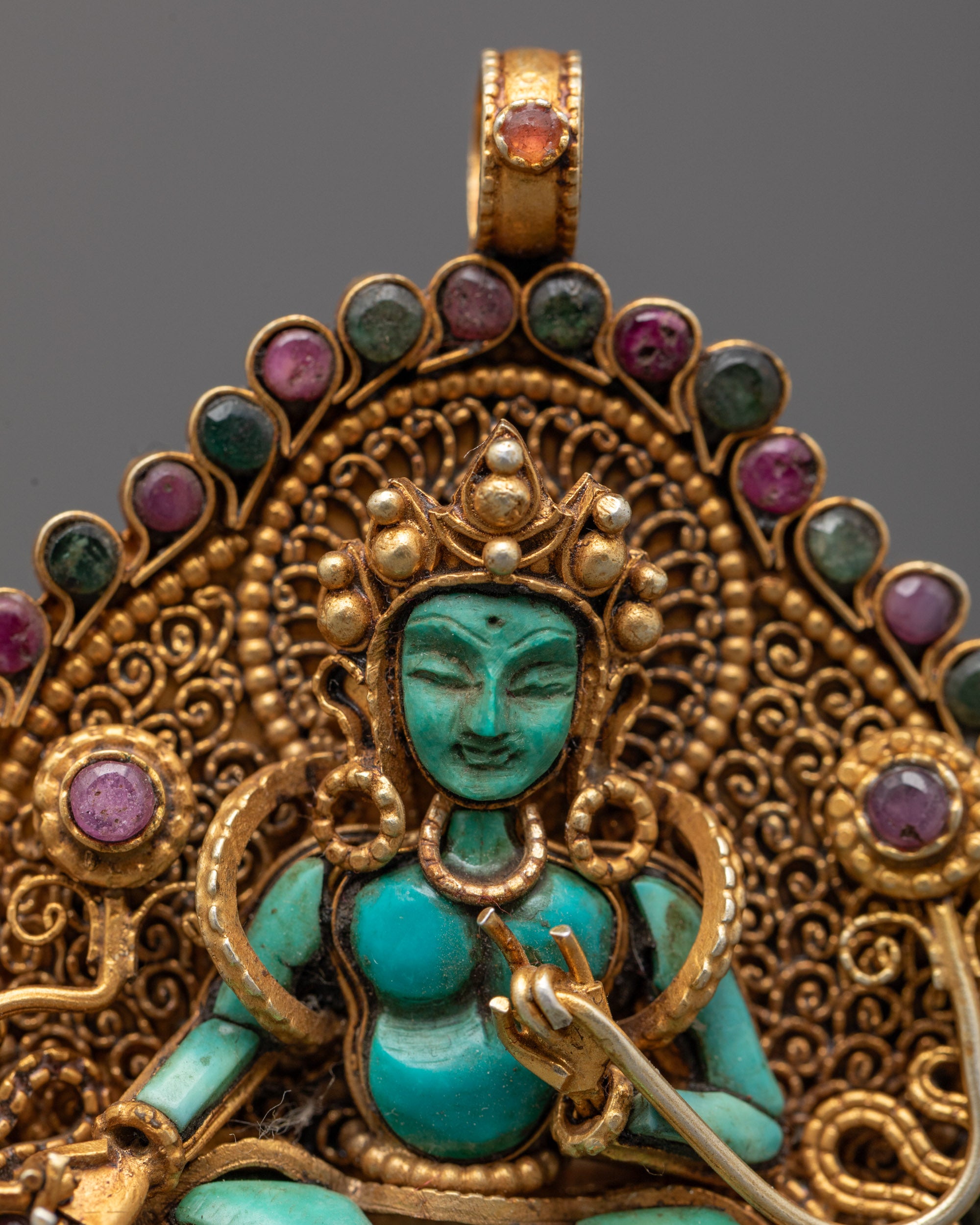 Close-up of hand-carved Green Tara holding utpala flower with coral center and gold details