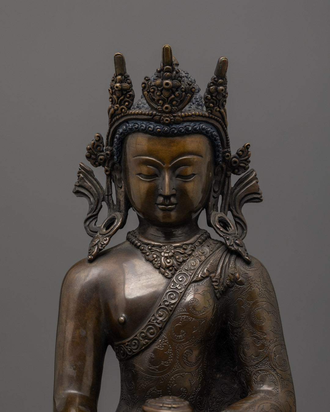 Close-up of oxidized copper face and intricate jewelry on Crowned Shakyamuni Buddha
