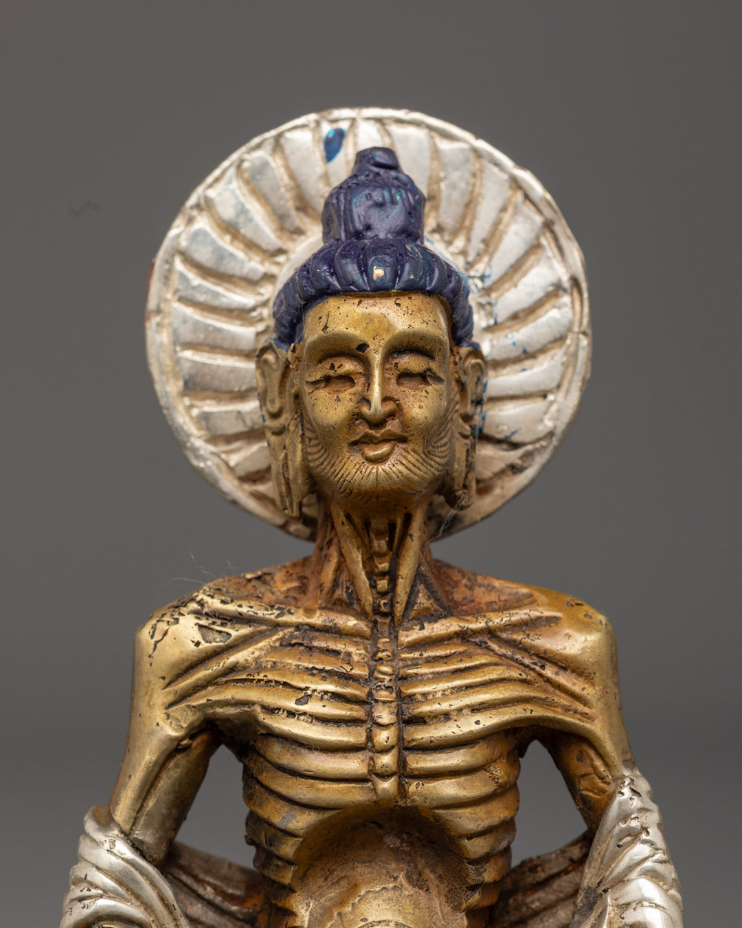 Emaciated Buddha statue showcasing sunken ribs and a serene facial expression with a traditional electroplating finish