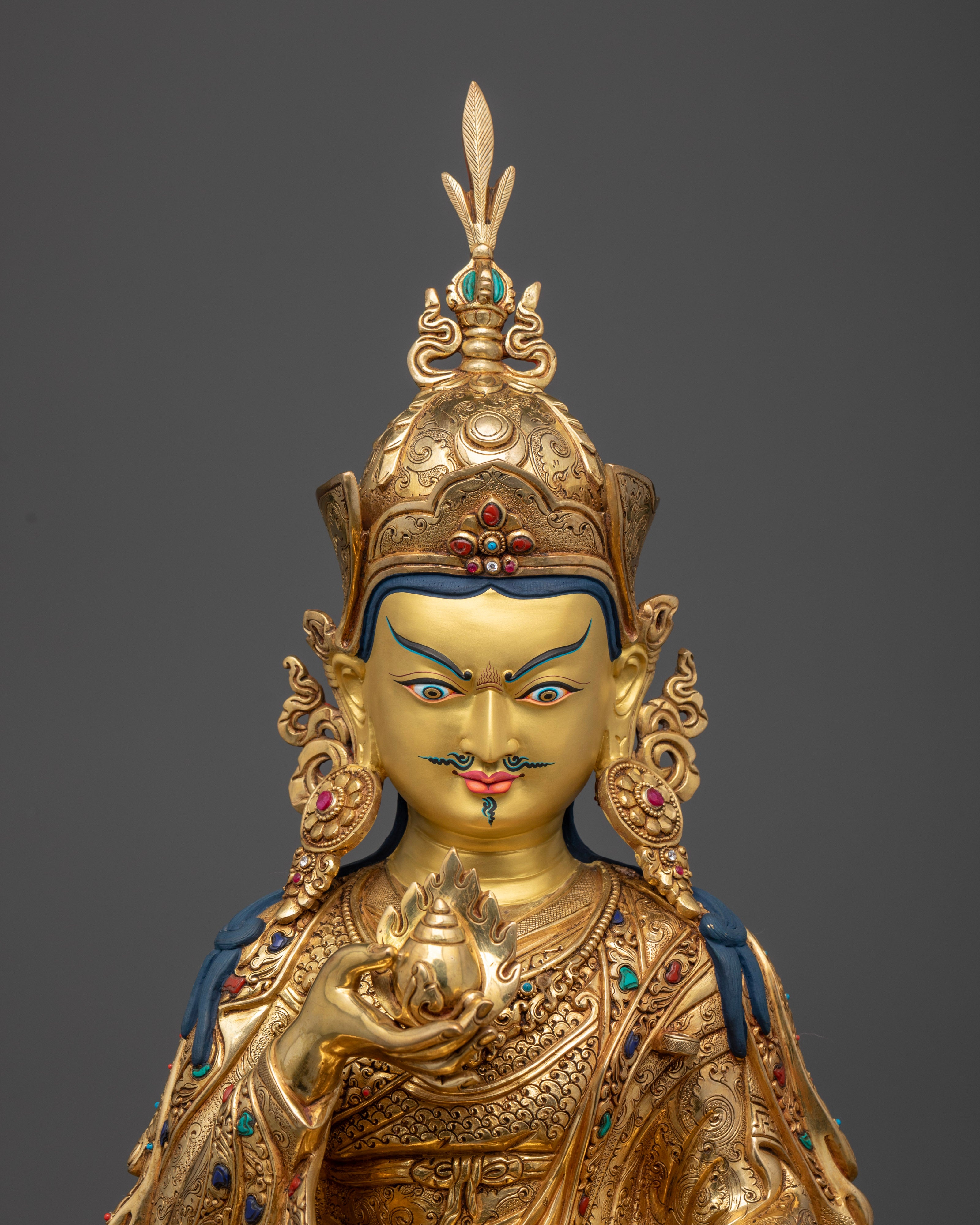 Close up Guru Norlha gold-painted face with lotus hat and vulture feather, hand-carved Himalayan sculpture