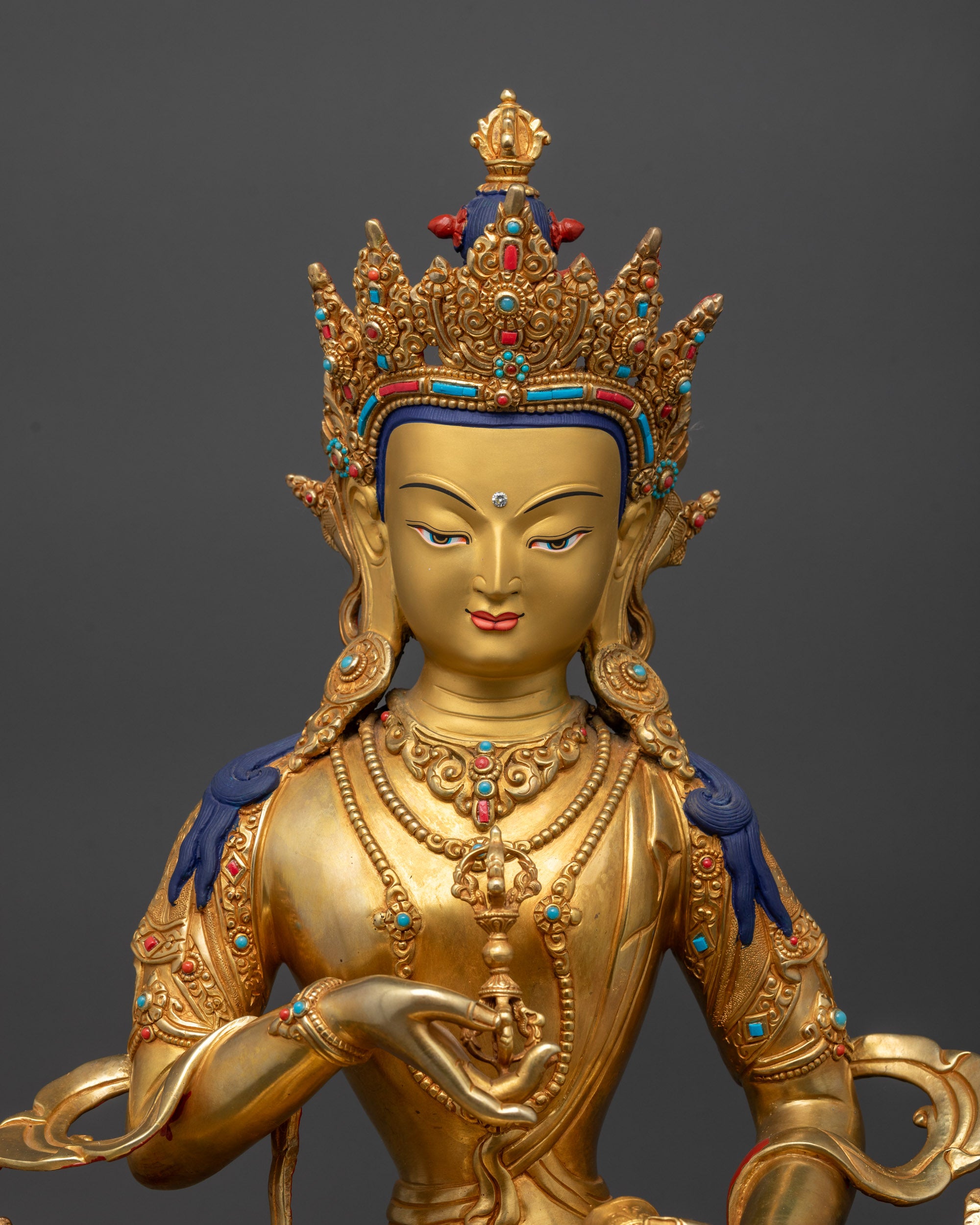 Close up Vajrasattva statue showing vajra, bell, gemstones, and intricate crown details