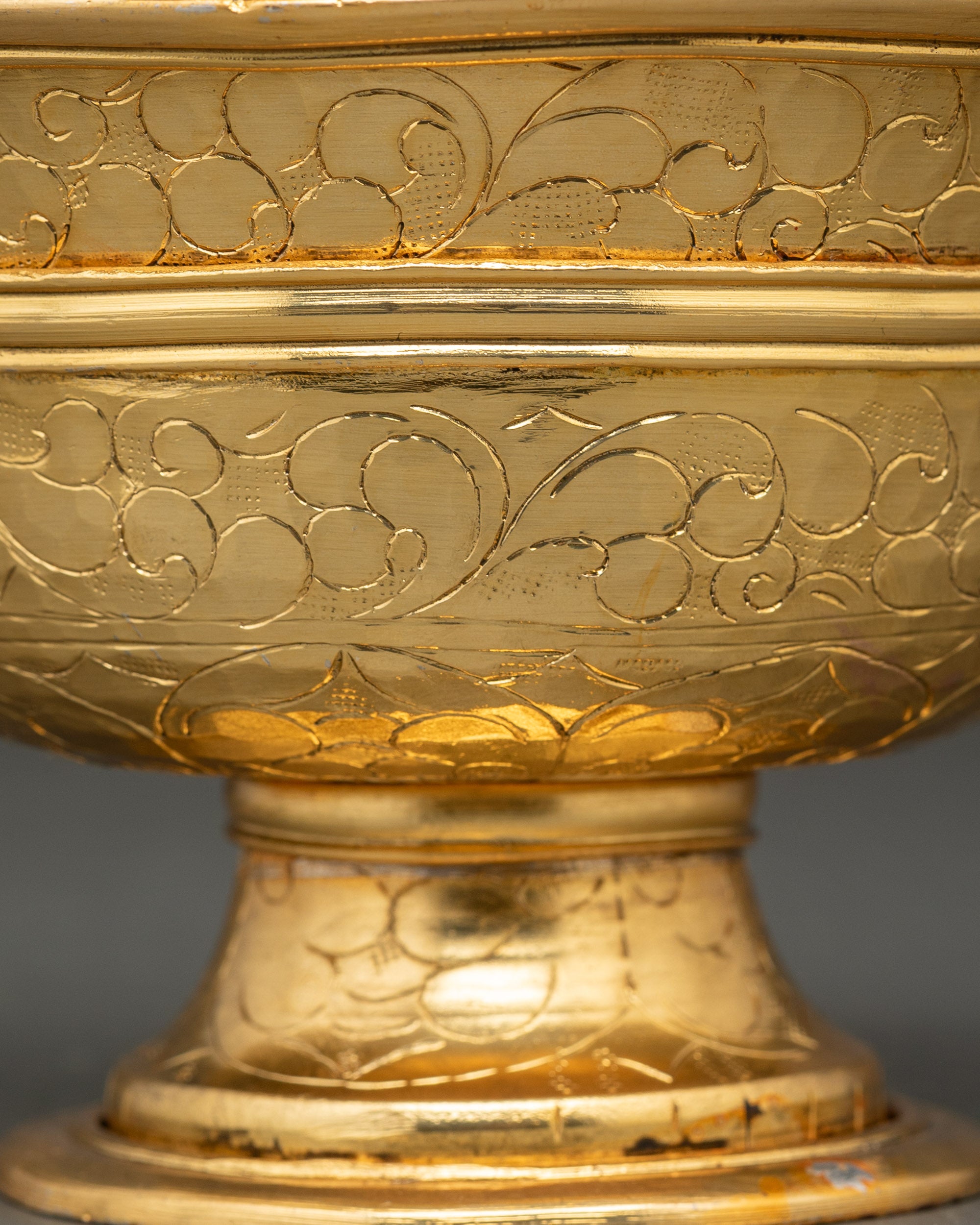 Close up gold and silver-plated water offering bowl with intricate floral motifs