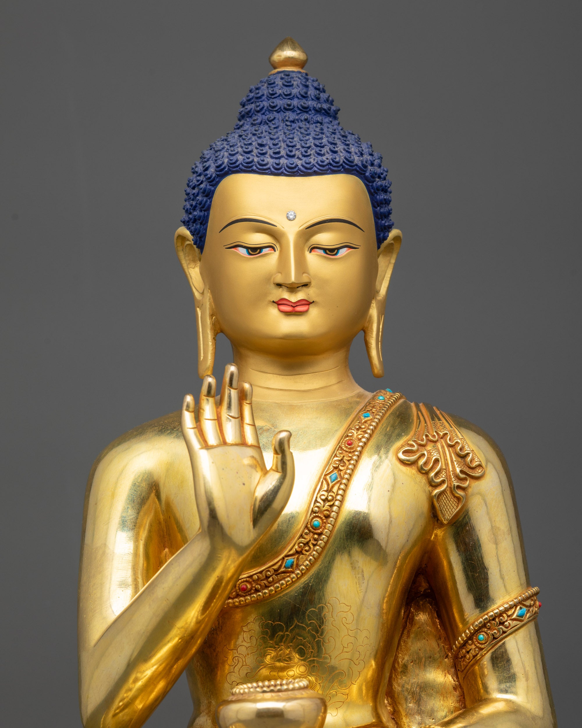 Close up of Amoghasiddhi Buddha statue showing serene gold-gilded face and polished finish