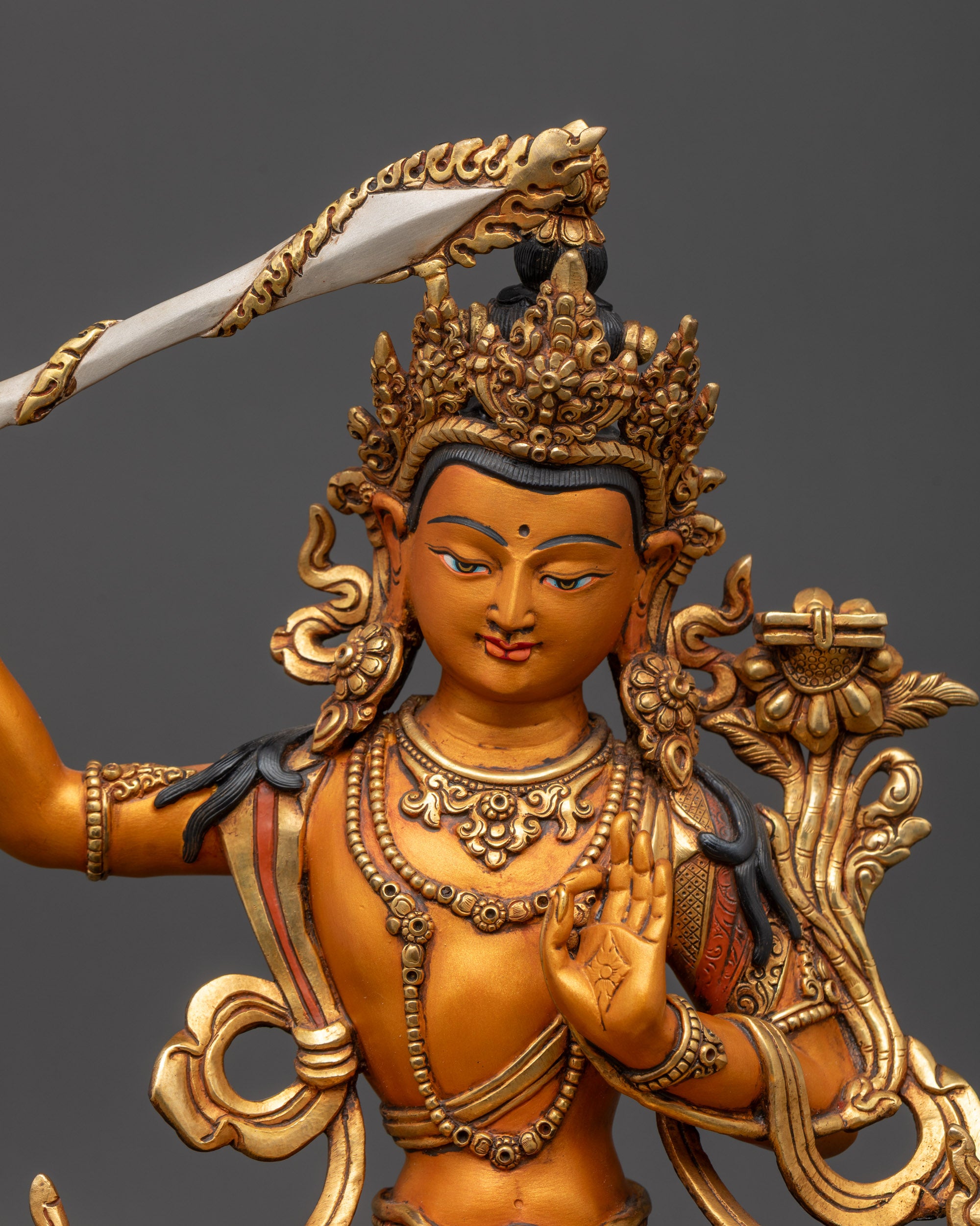 Close up of Manjushri gold-gilded face holding utpala flower and double-edged sword
