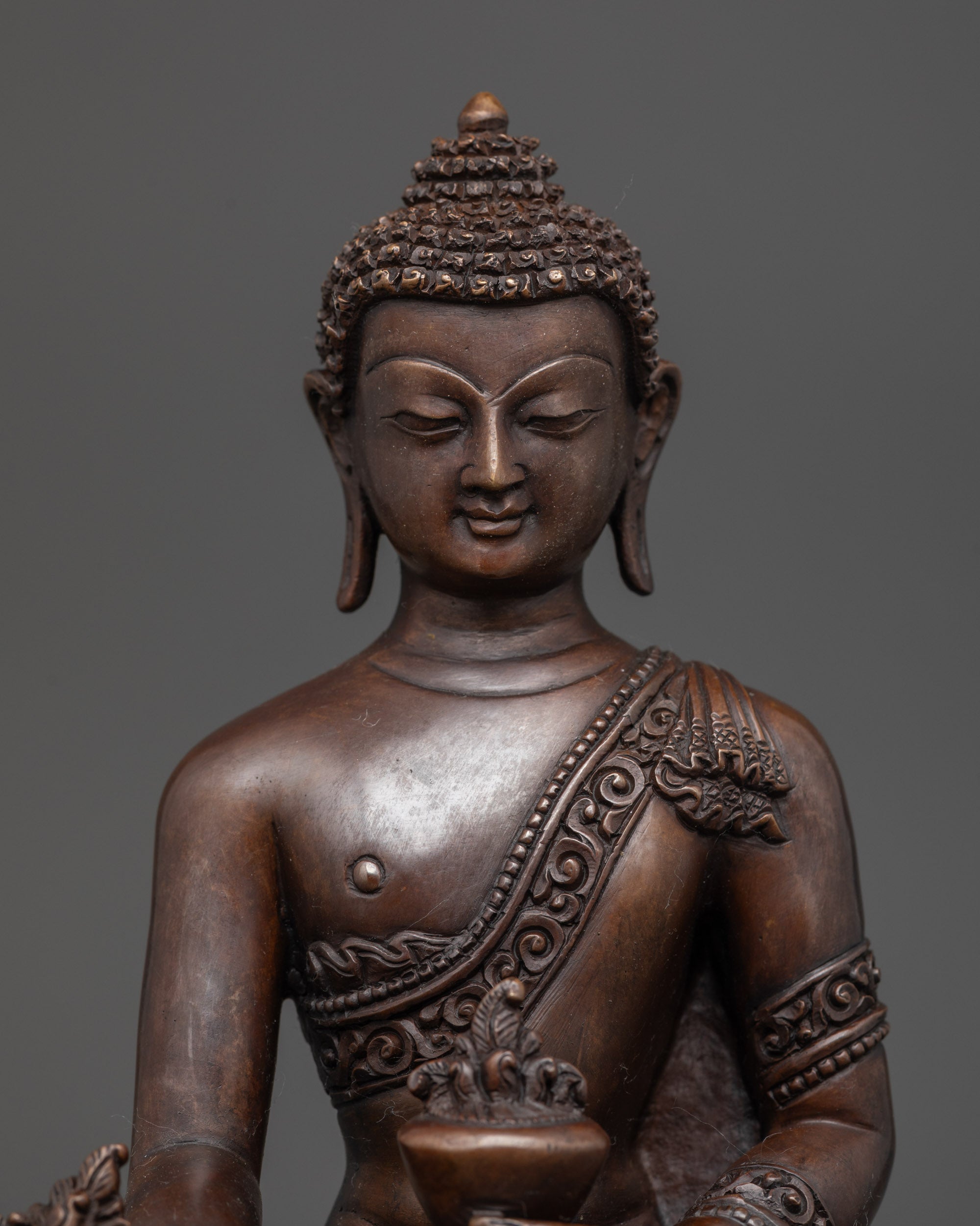 Close up of Medicine Buddha statue showing intricate details and earthy oxidized copper finish