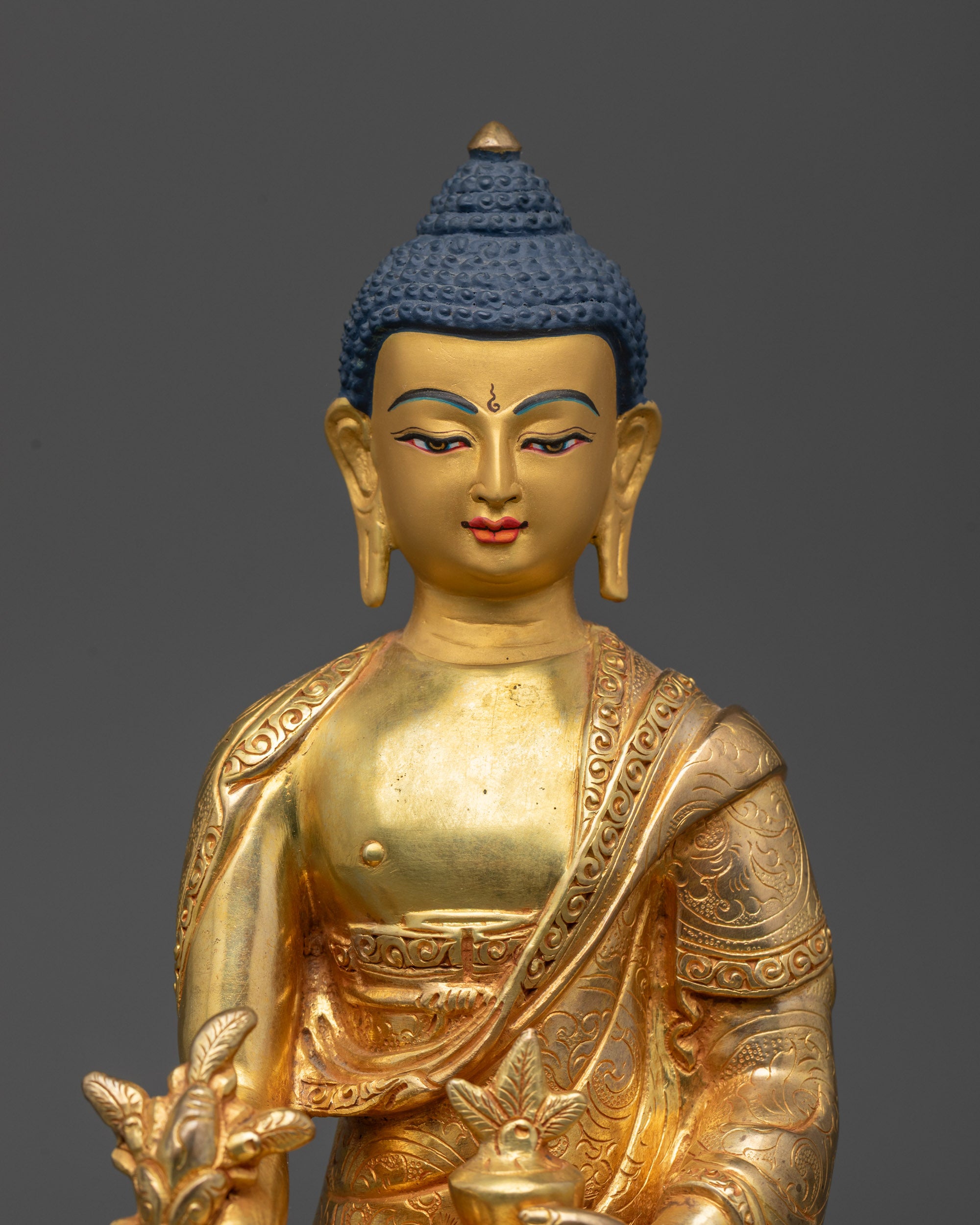 Close up of Medicine Buddha statue showing intricate robe patterns and semi-precious stones