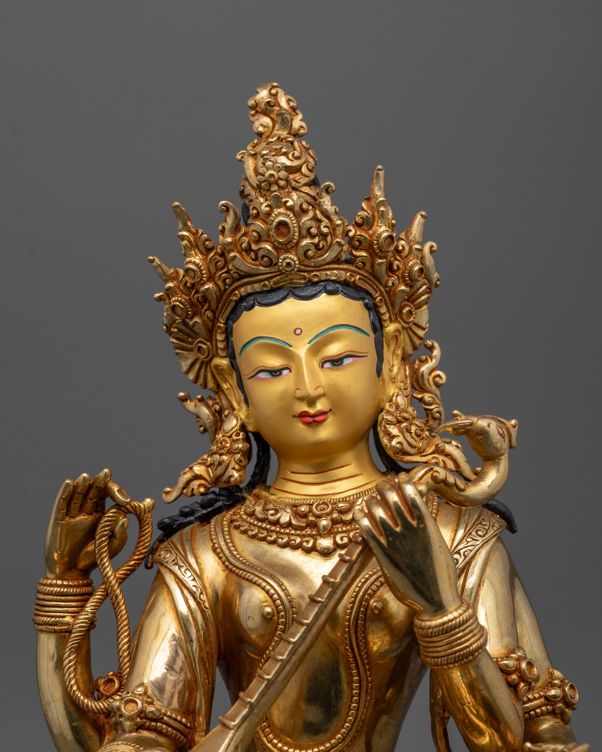 Close up of Saraswati Maa’s four arms holding veena, scriptures, and prayer beads with gold finish.