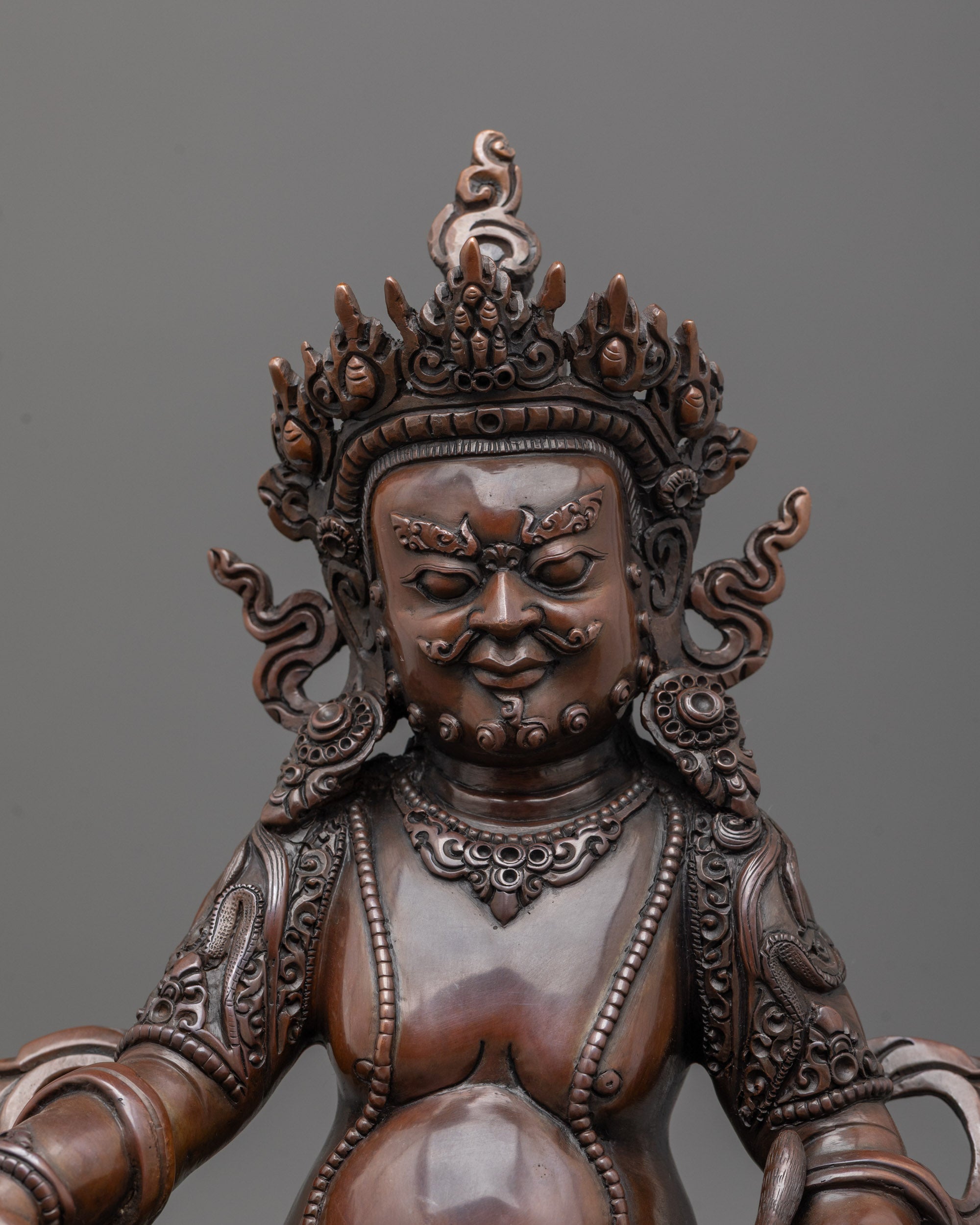 Close up of fierce oxidized copper face and intricate carved patterns on robes of Dzambhala