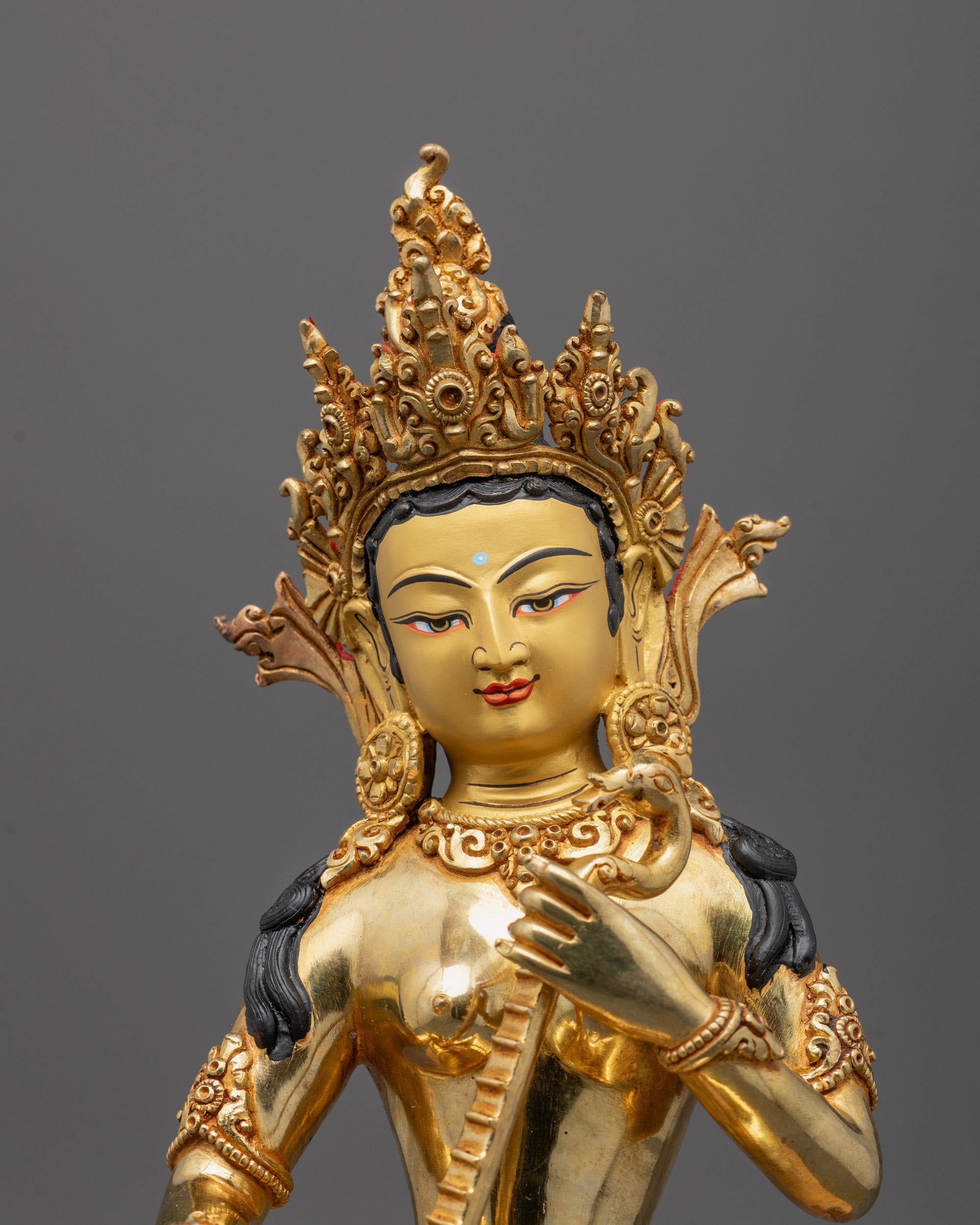 Close up of intricate carvings on Saraswati statue’s gold fire-gilded body and veena details