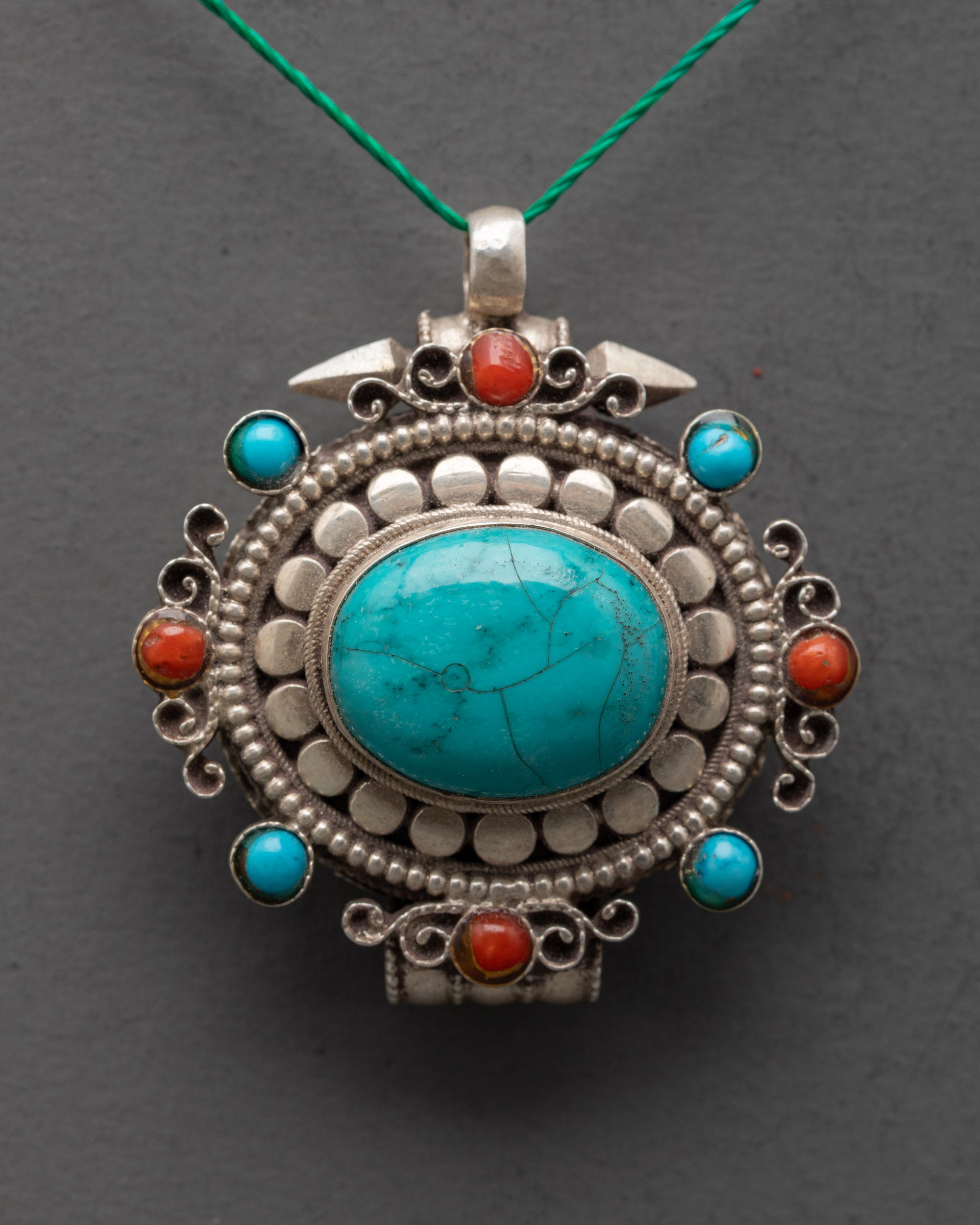 Close up of oval turquoise pendant showing coral gems and detailed silver carving work