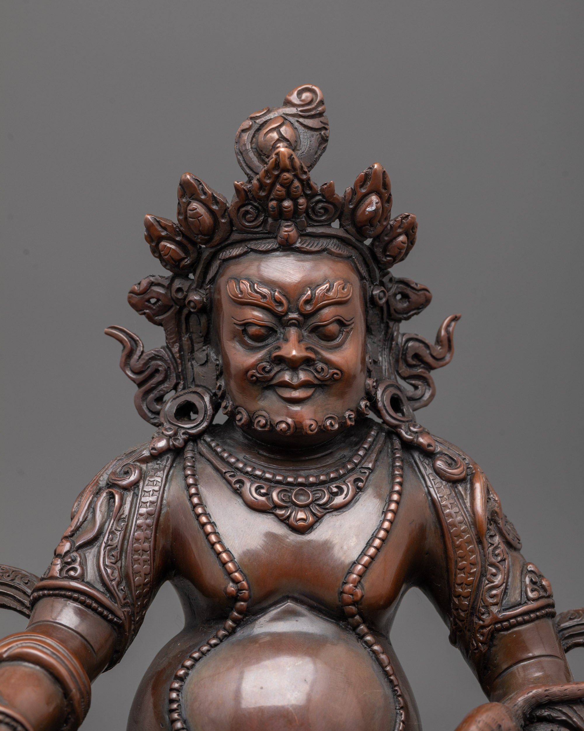 Close up of oxidized copper face and intricate robes on Dzambhala wealth deity statue