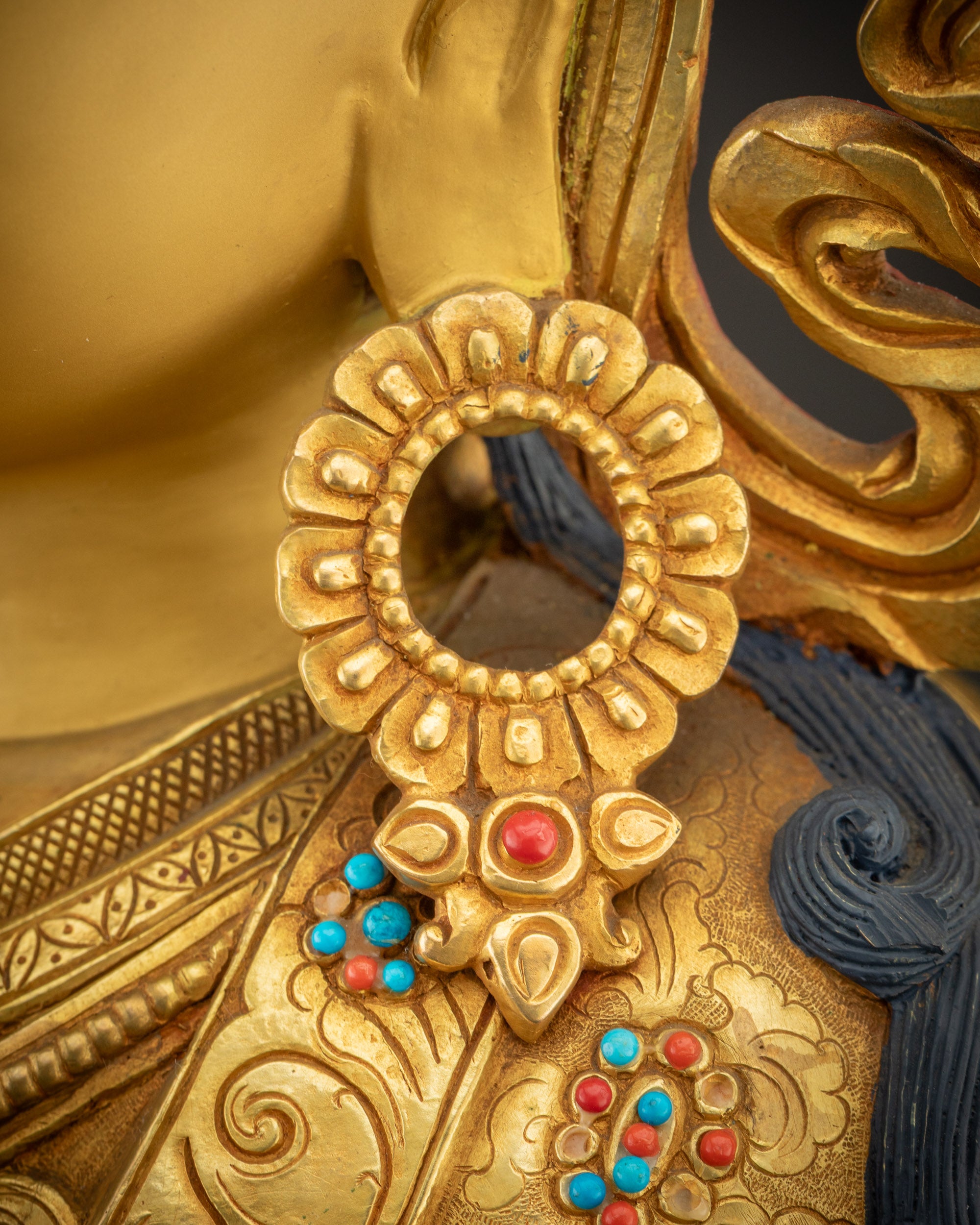 Close up of right earring of Guru Rinpoche showing gold and jewel details