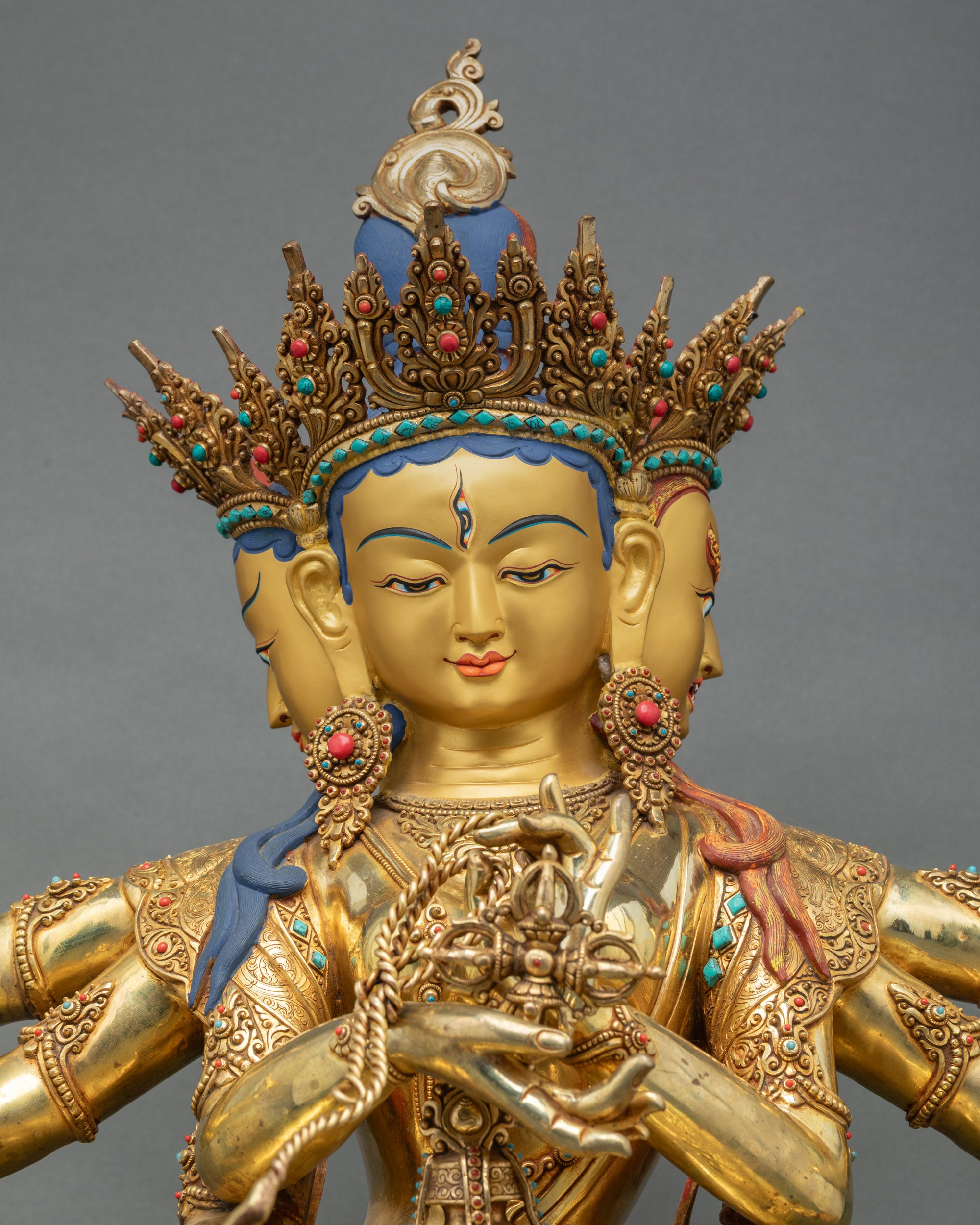 Close up three-faced Namgyalma gold-painted face adorned with turquoise and coral