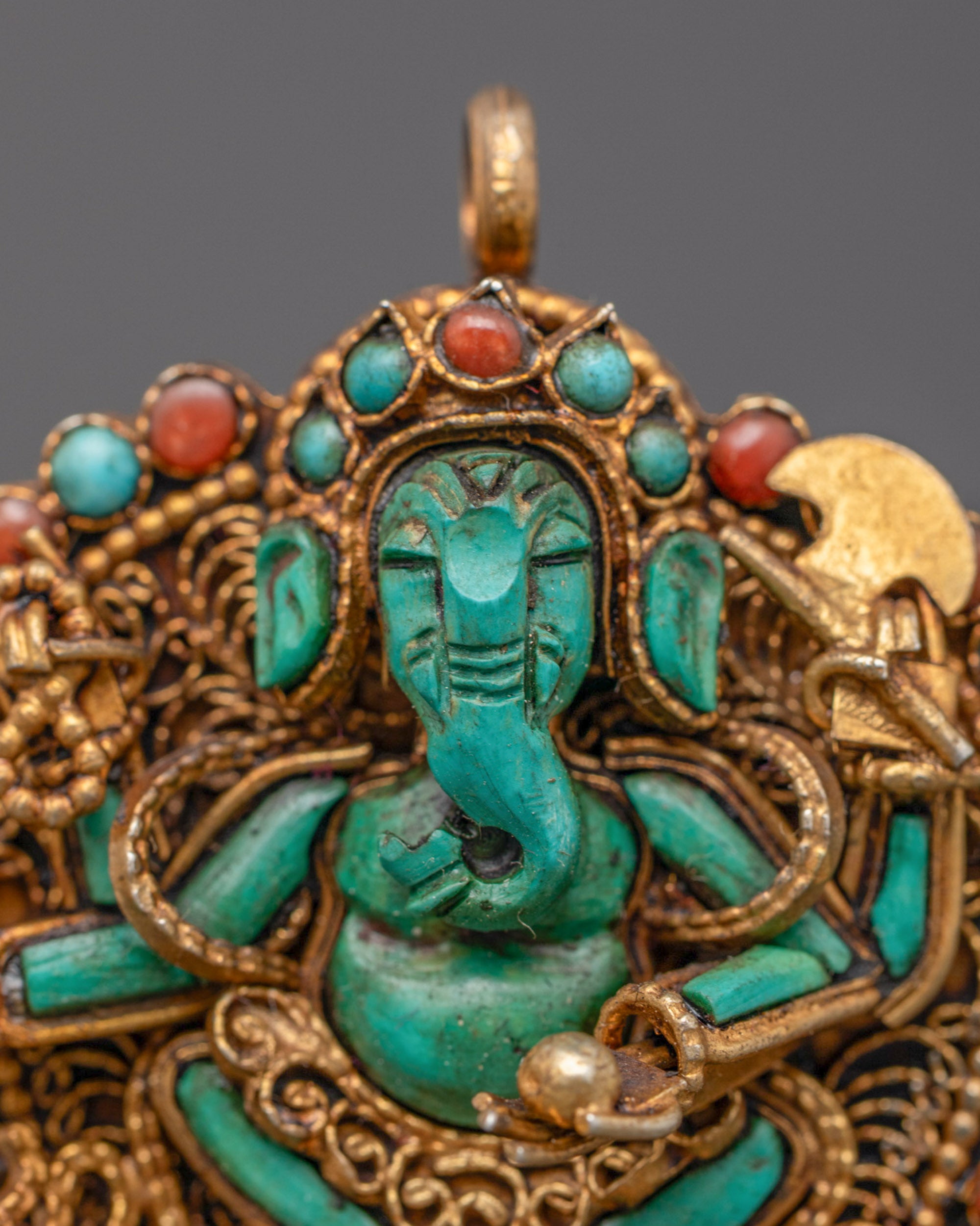 Closeup of Ganesha pendant showing intricate filigree work and four-armed turquoise figure