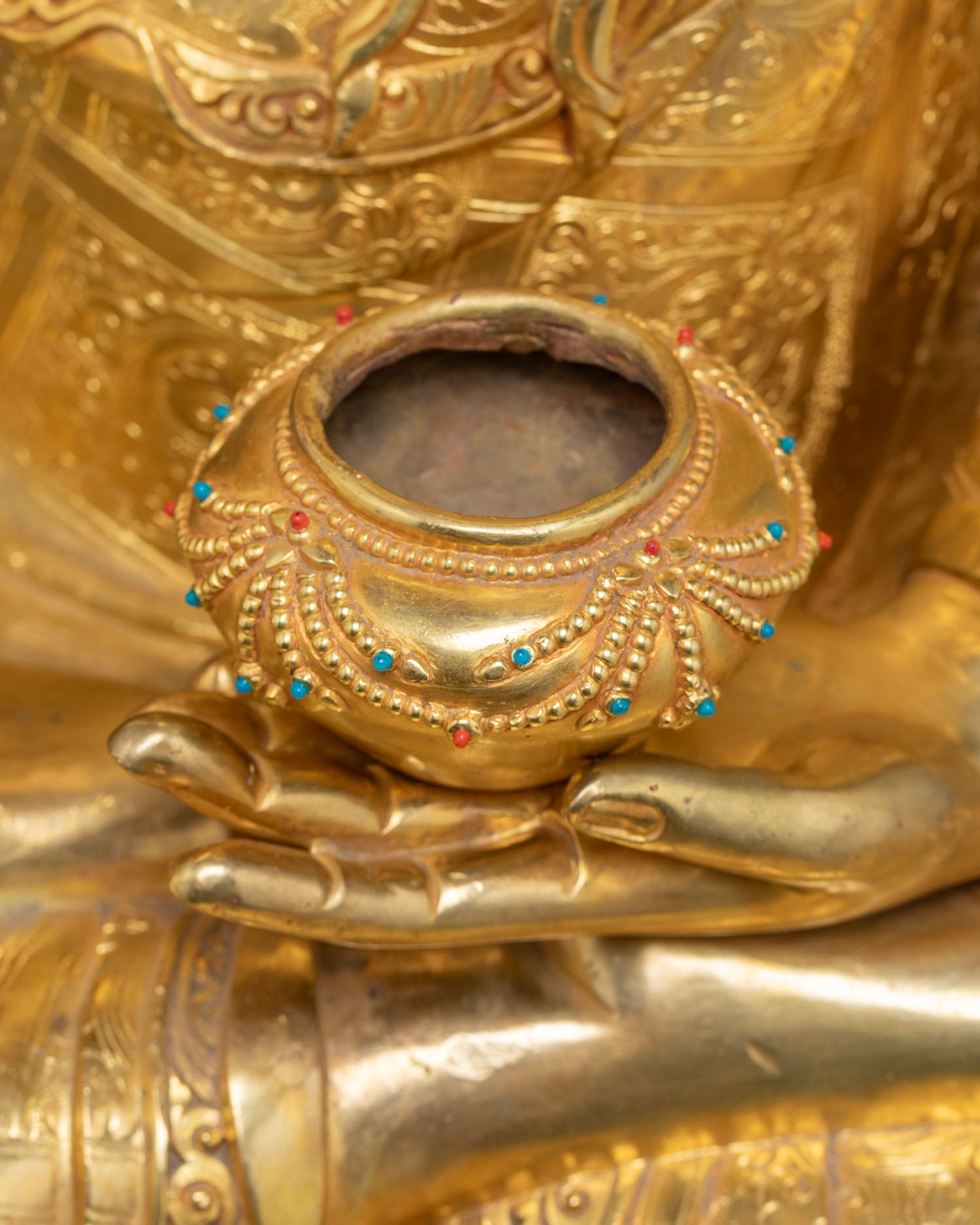 Detailed close-up of gemstone-inlaid Patra bowl in hand of Shakyamuni Buddha