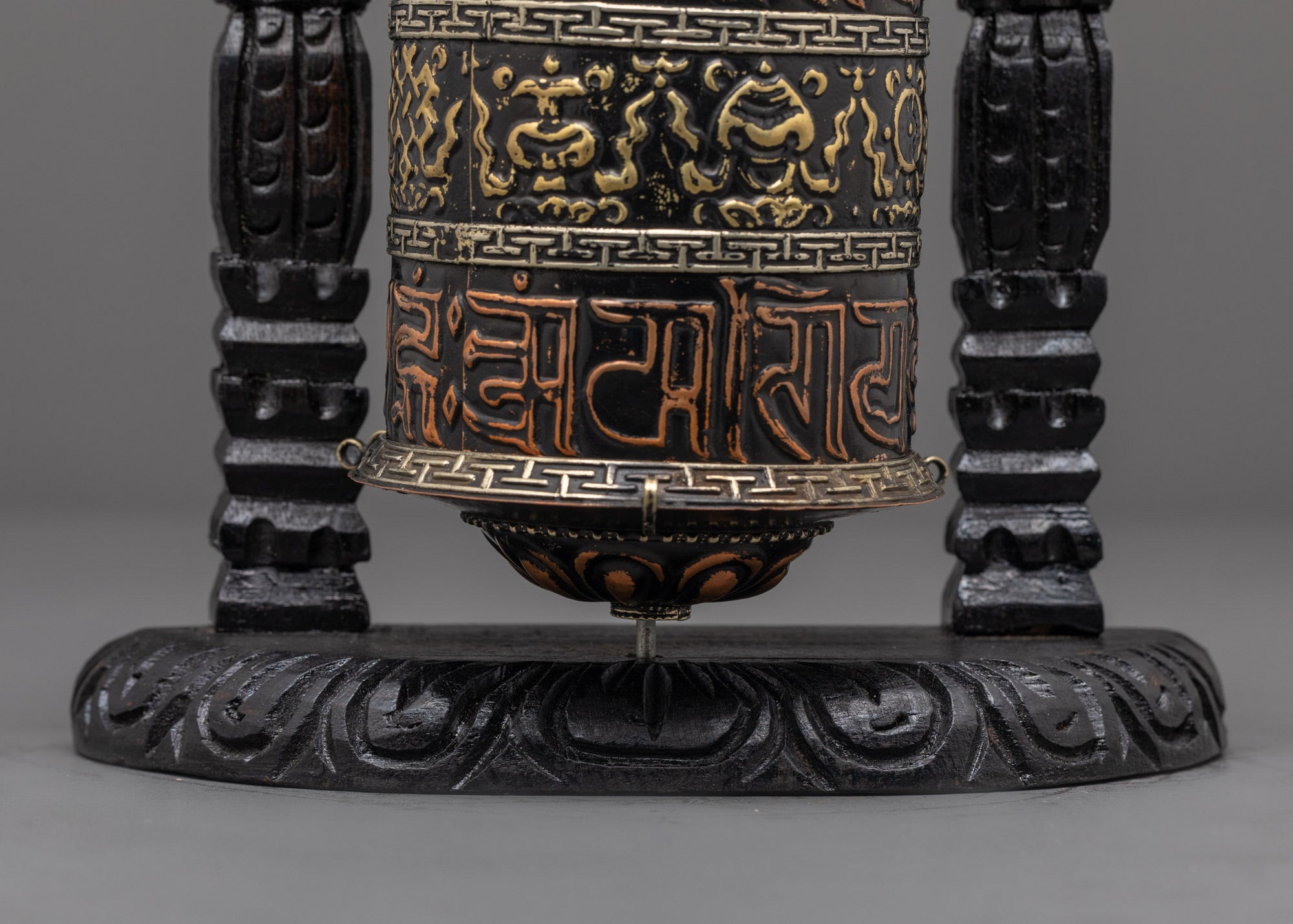 Detailed bronze finish patterns and white metal auspicious symbols on prayer wheel