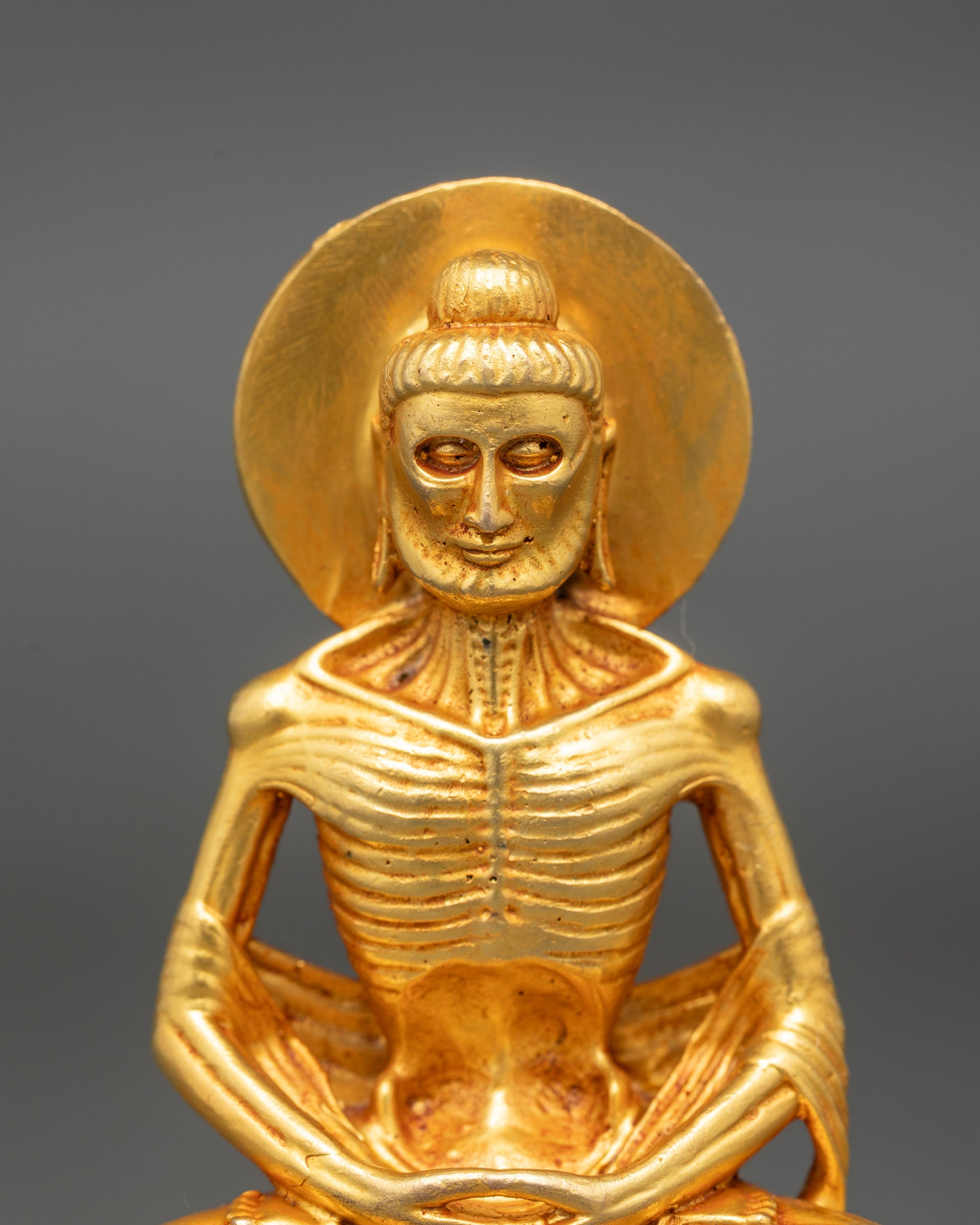 Detailed close-up of Fasting Buddha face showing serene expression and gold-painted finish