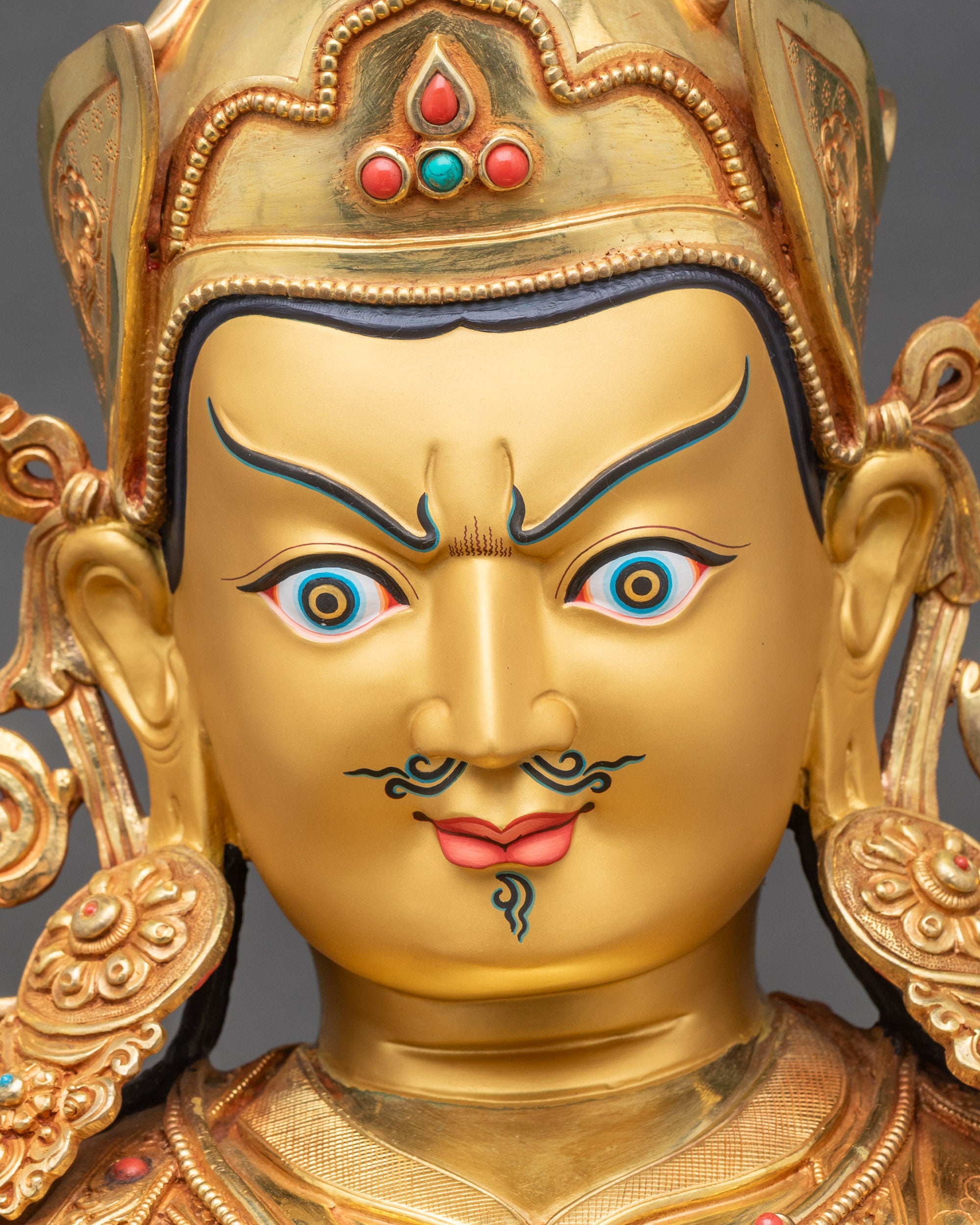 Detailed close-up of Guru Rinpoche face, expressive features, gold fire-gilded finish
