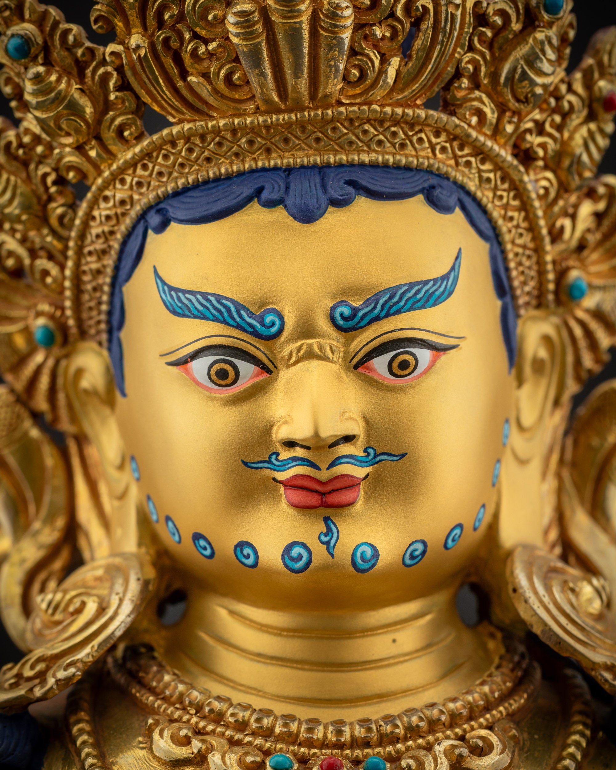 Detailed close up face Dzambhala statue gold-gilded with piercing eyes and lush blue eyebrows