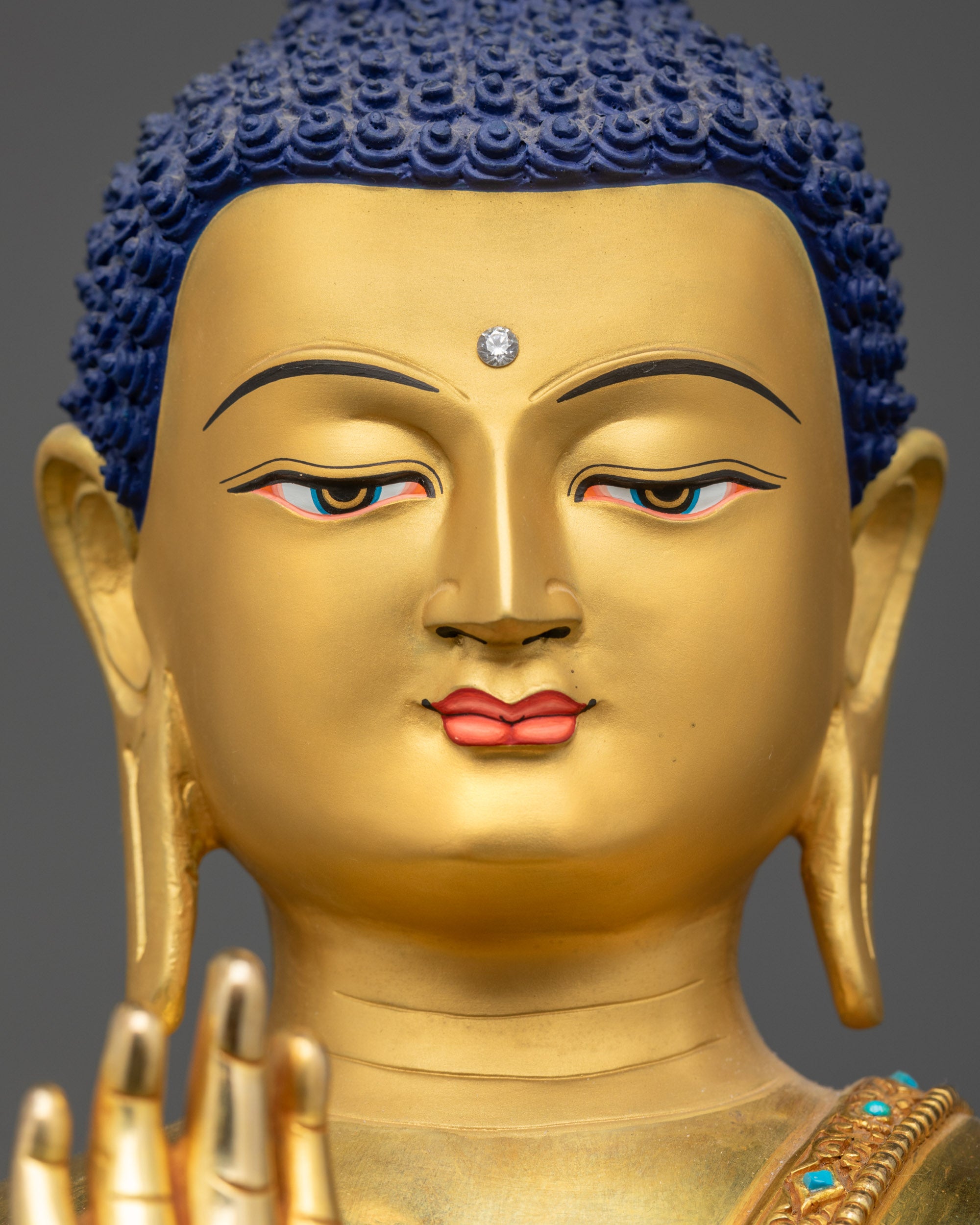 Detailed close up face of Amoghasiddhi Buddha statue with gold-gilded features and stones