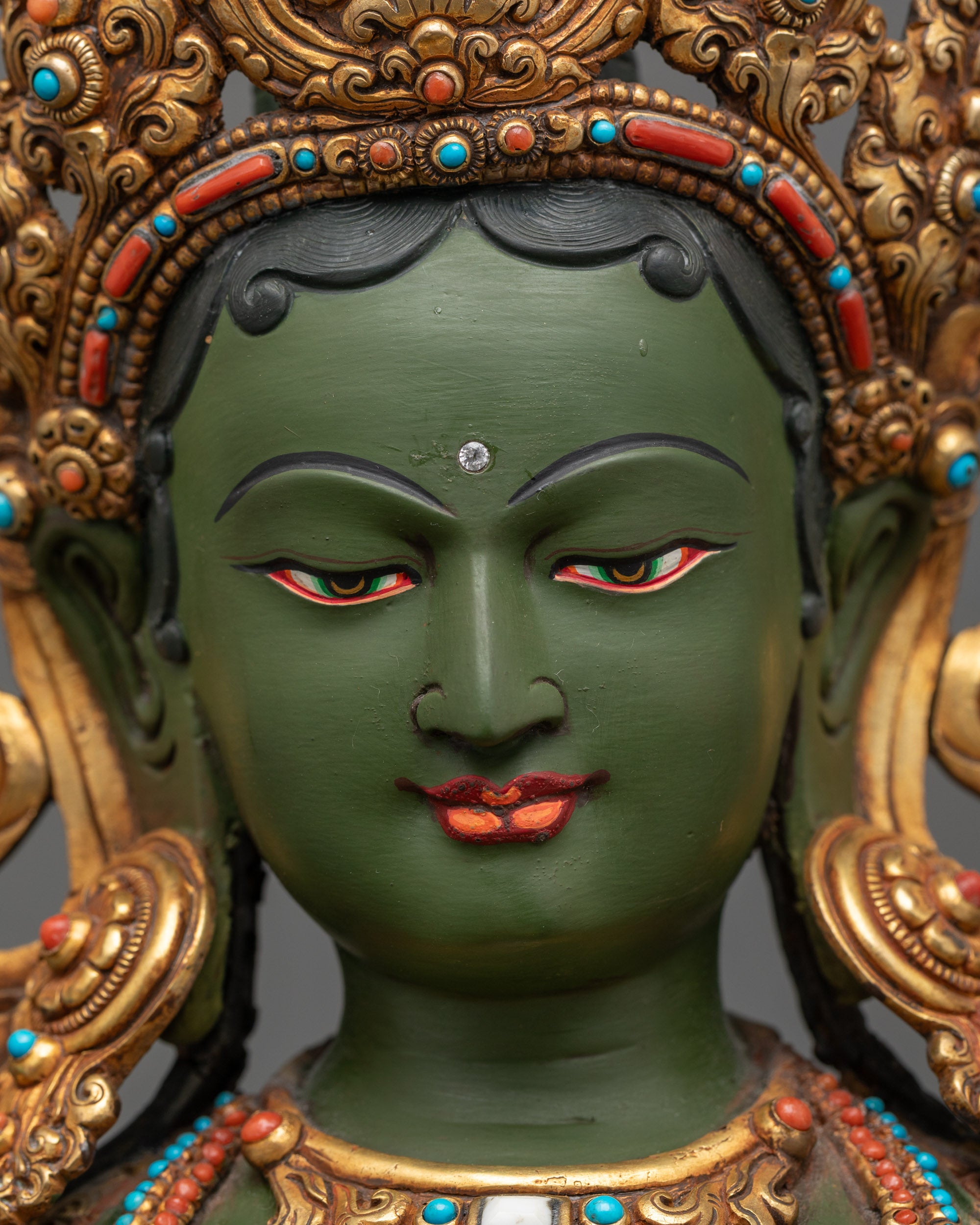 Detailed close up face of Green Tara statue with semi-precious crown and serene expression