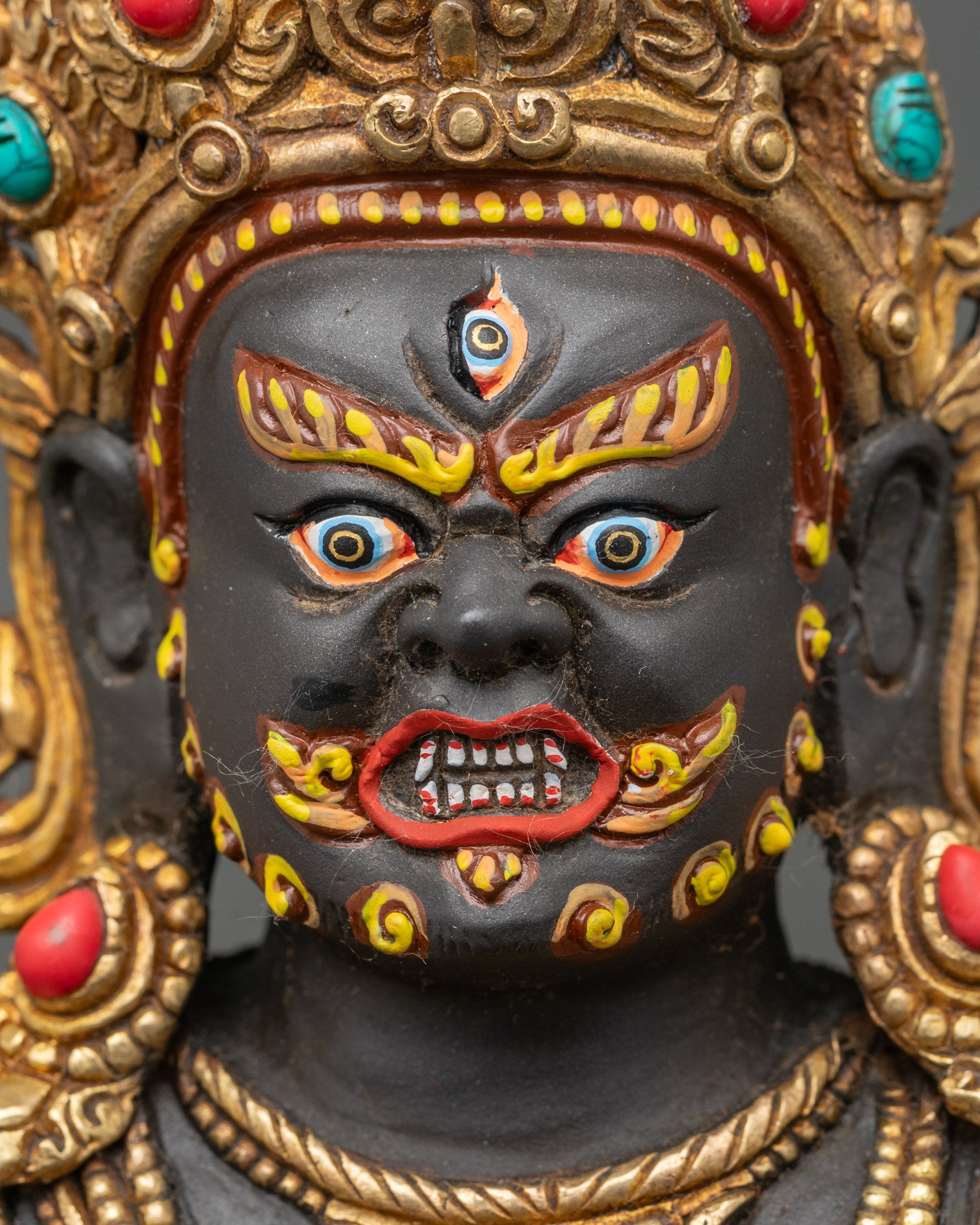 Detailed face close-up of Black Dzambhala deity, gold-gilded and vividly painted