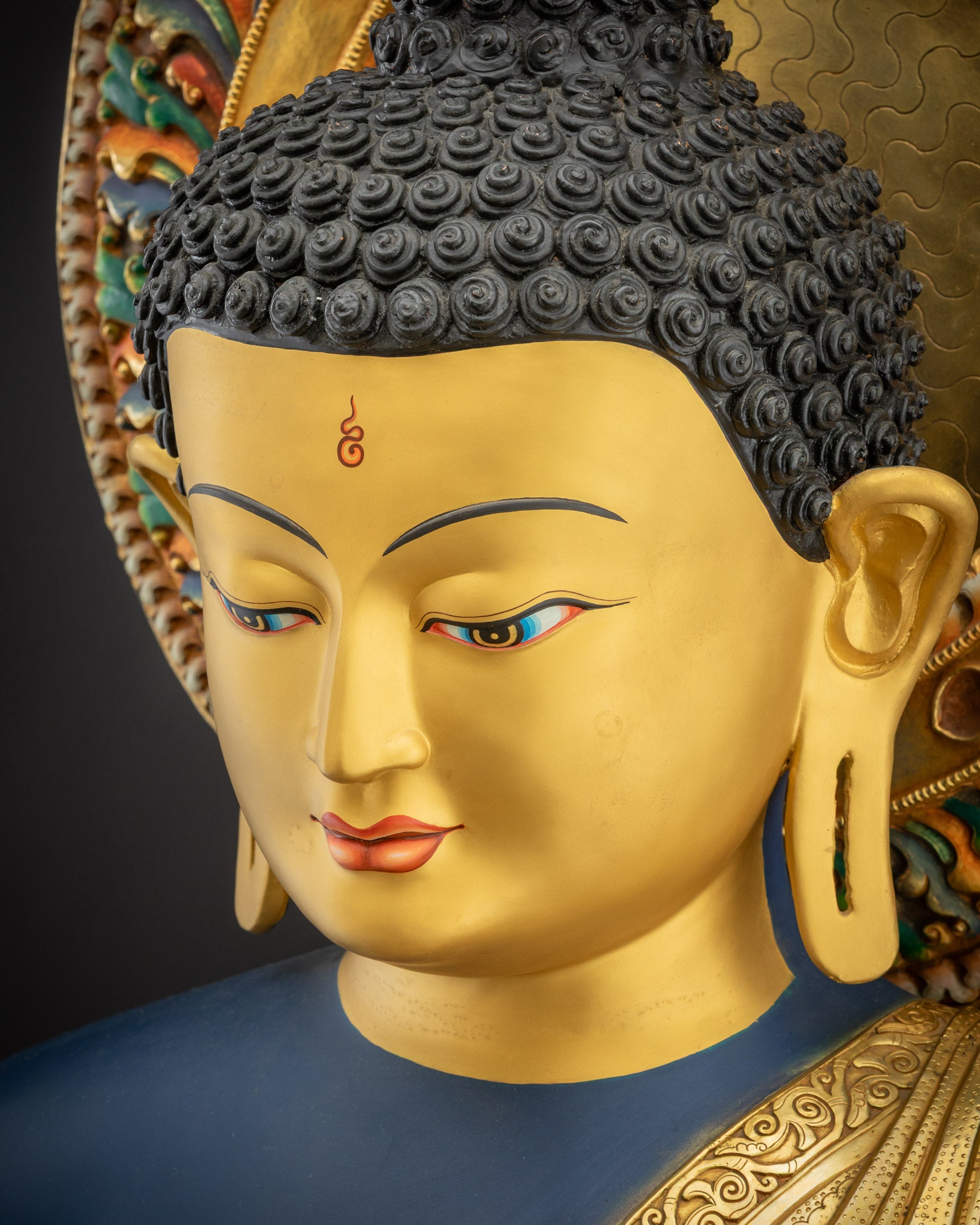 Detailed upper close up of face of Medicine Buddha Statue showing serene expression and gilding