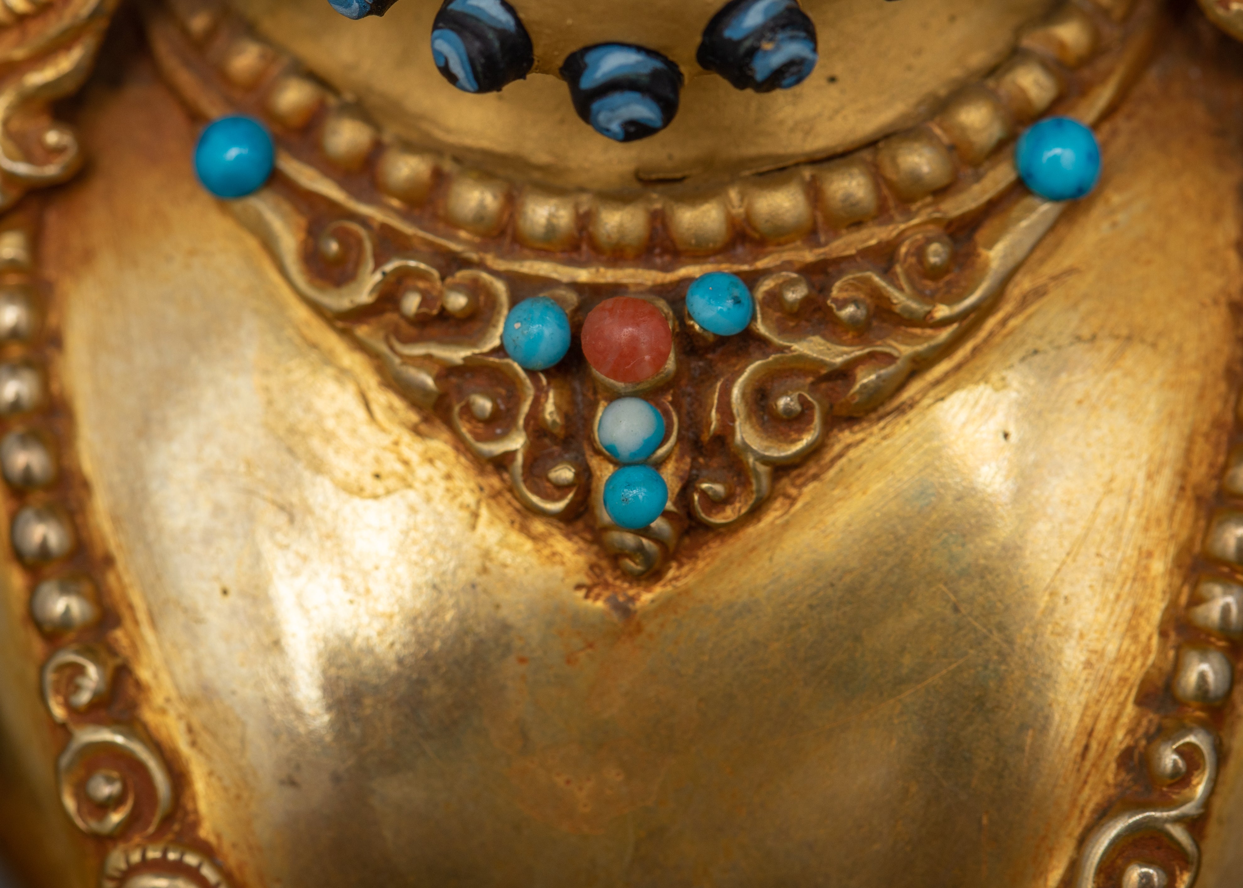 Close-up view of Dzambhala’s necklace adorned with turquoise and coral stones.