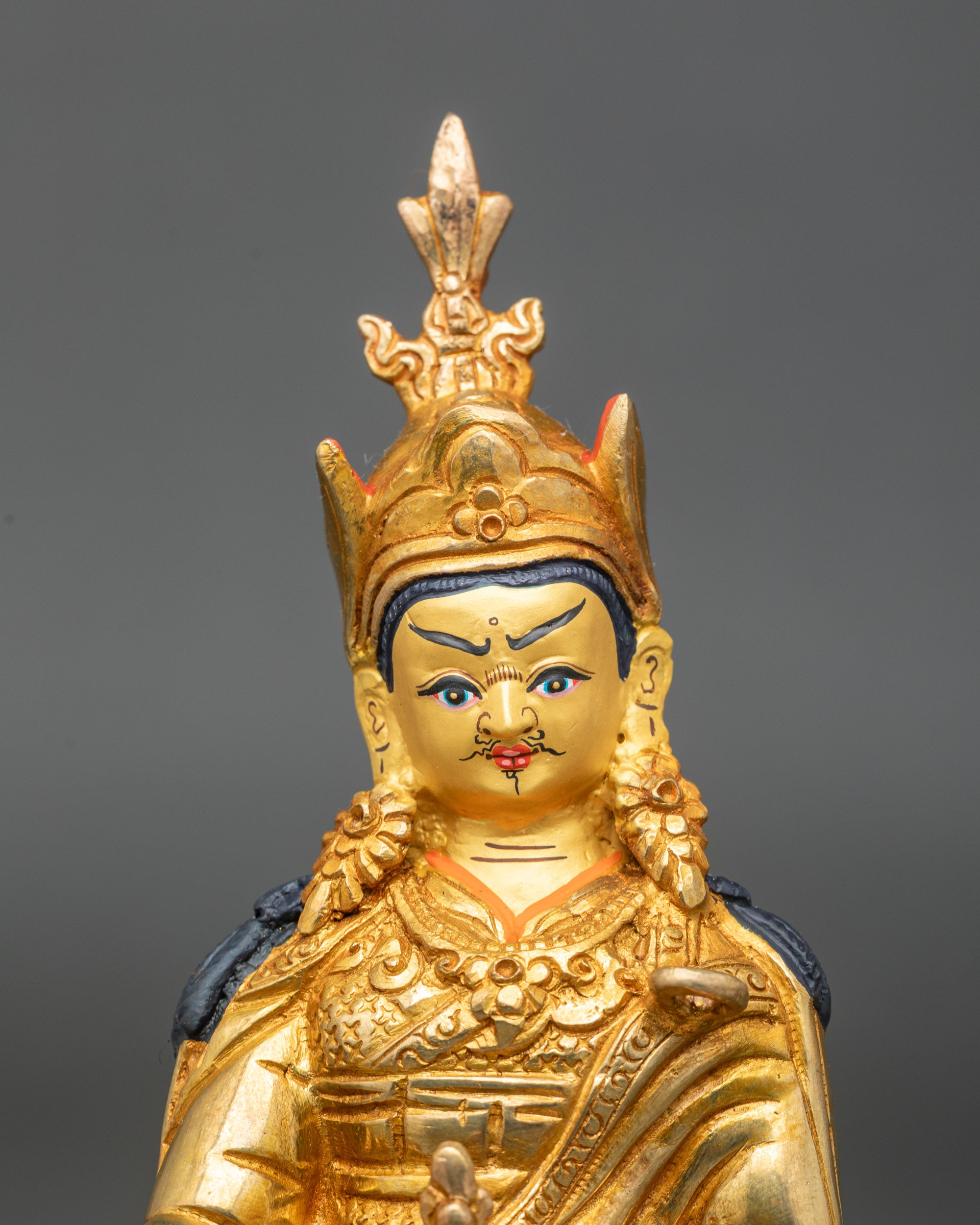 Close-up of Guru Rinpoche statue showing intricate gold fire-gilded details and polished finish
