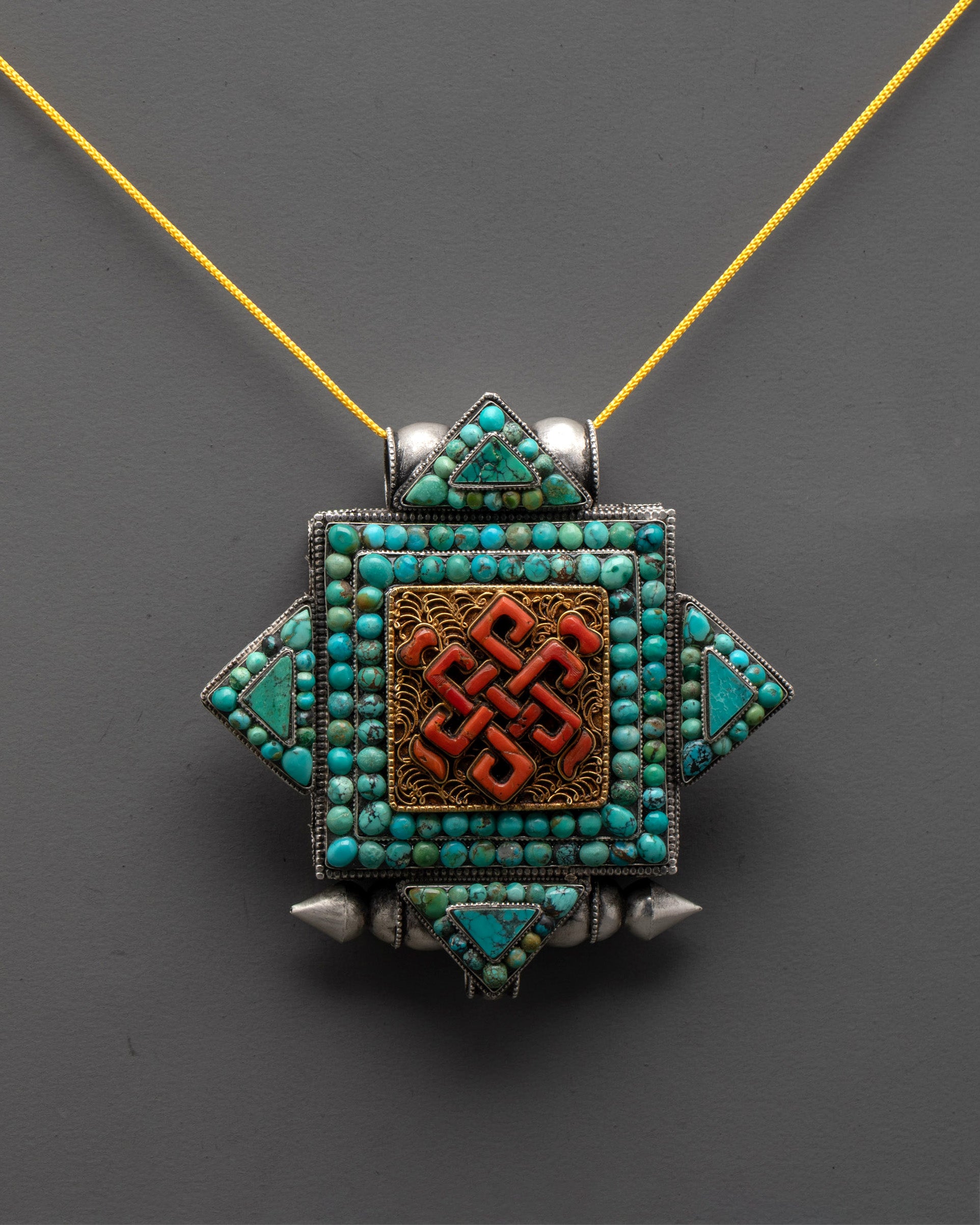 Front view of Endless Knot Locket with coral turquoise stones and gold-plated filigree design