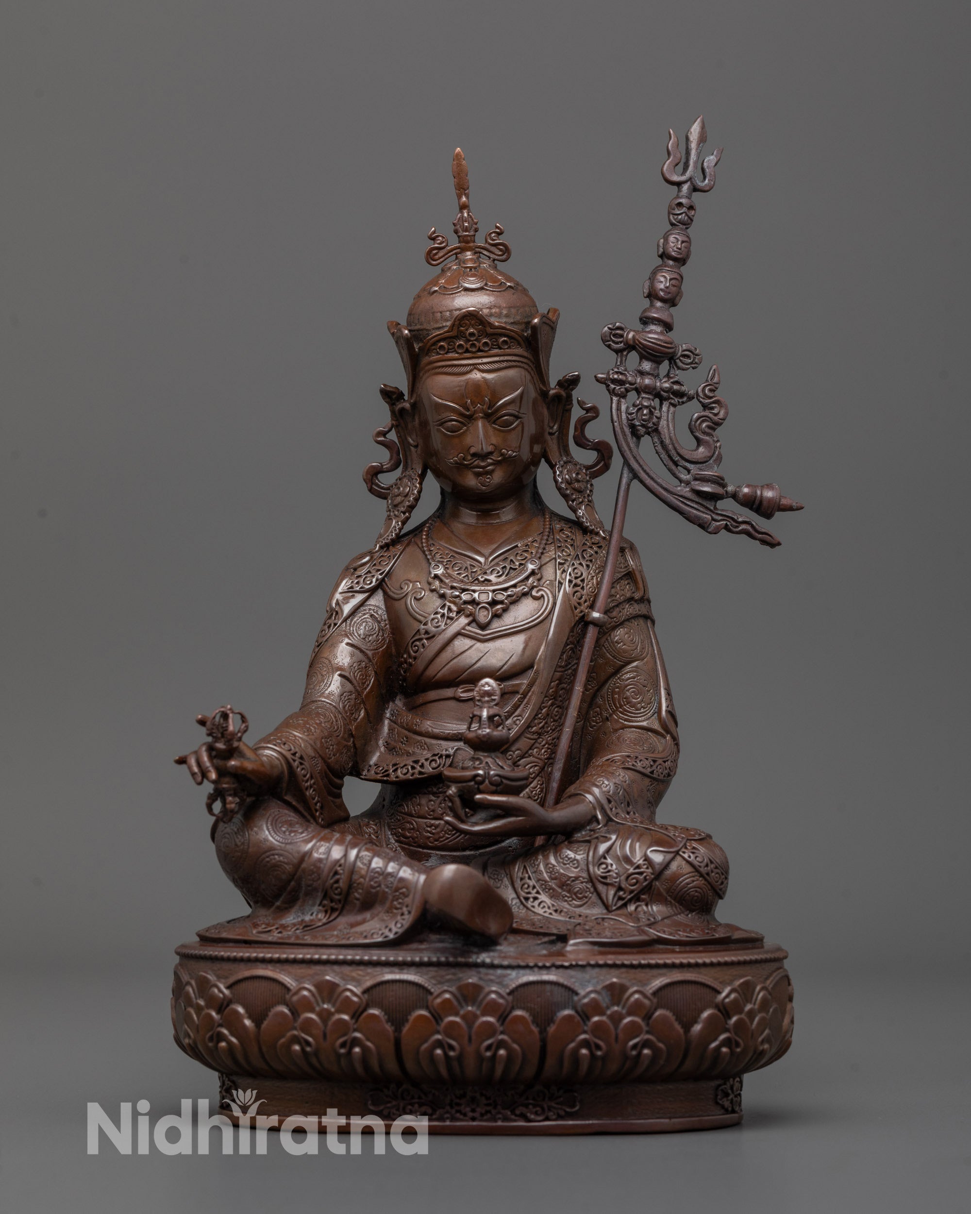 Front view of Guru Rinpoche statue seated on lotus base with vajra and skull cup