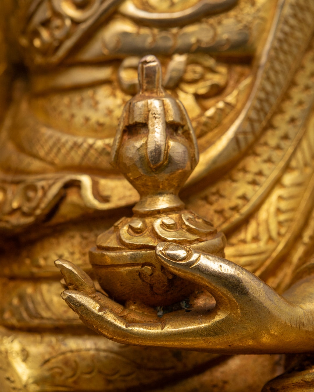 Guru Rinpoche sculpture seated in meditation pose, holding vajra and skull cup, surrounded by colorful ornamentation.